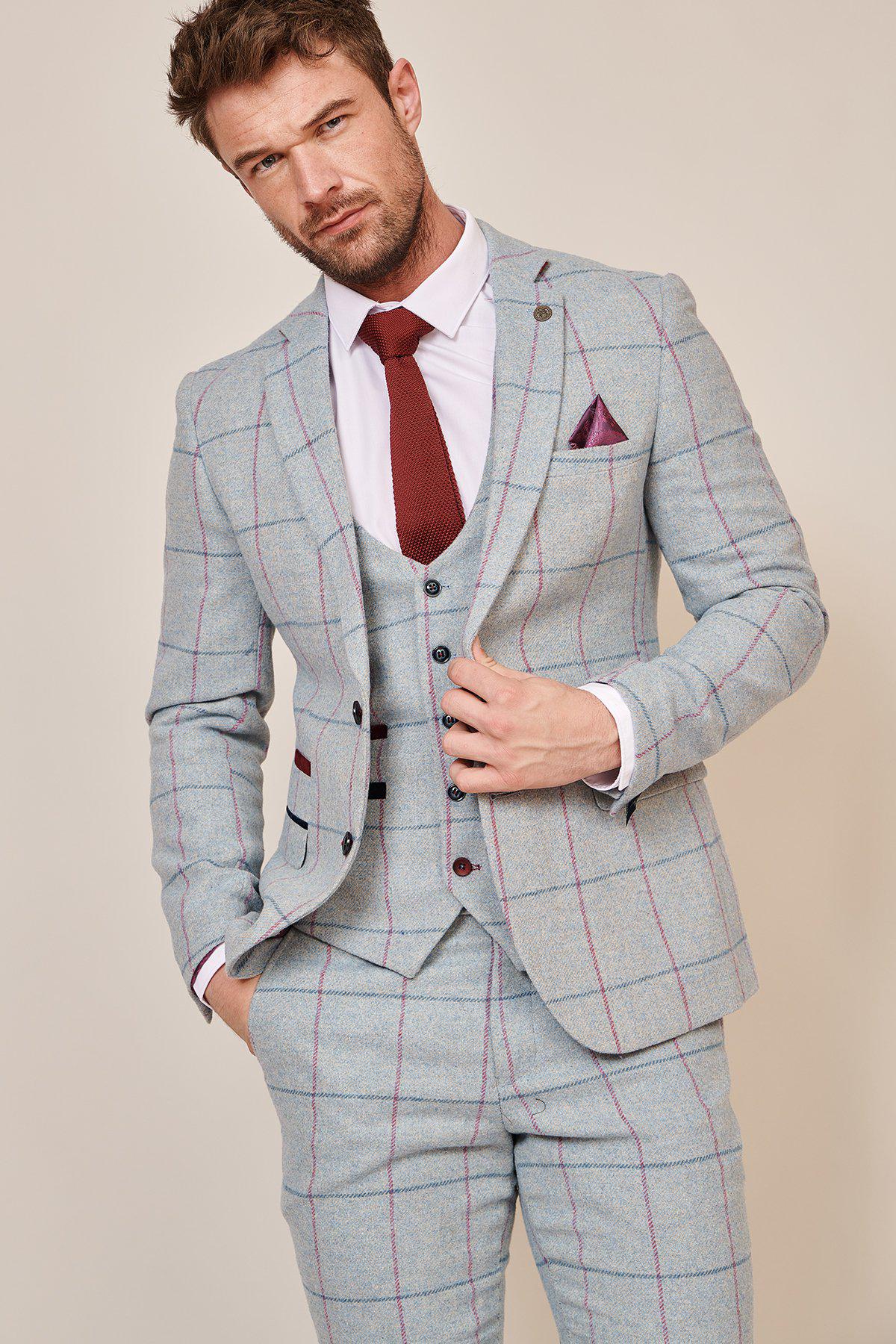 A man with short brown hair and a trimmed beard wears the Marc Darcy NICOLAS - Sky Check Tweed Blazer with a white shirt, burgundy tie, and matching pocket square, standing against a plain background holding his jacket lapel.