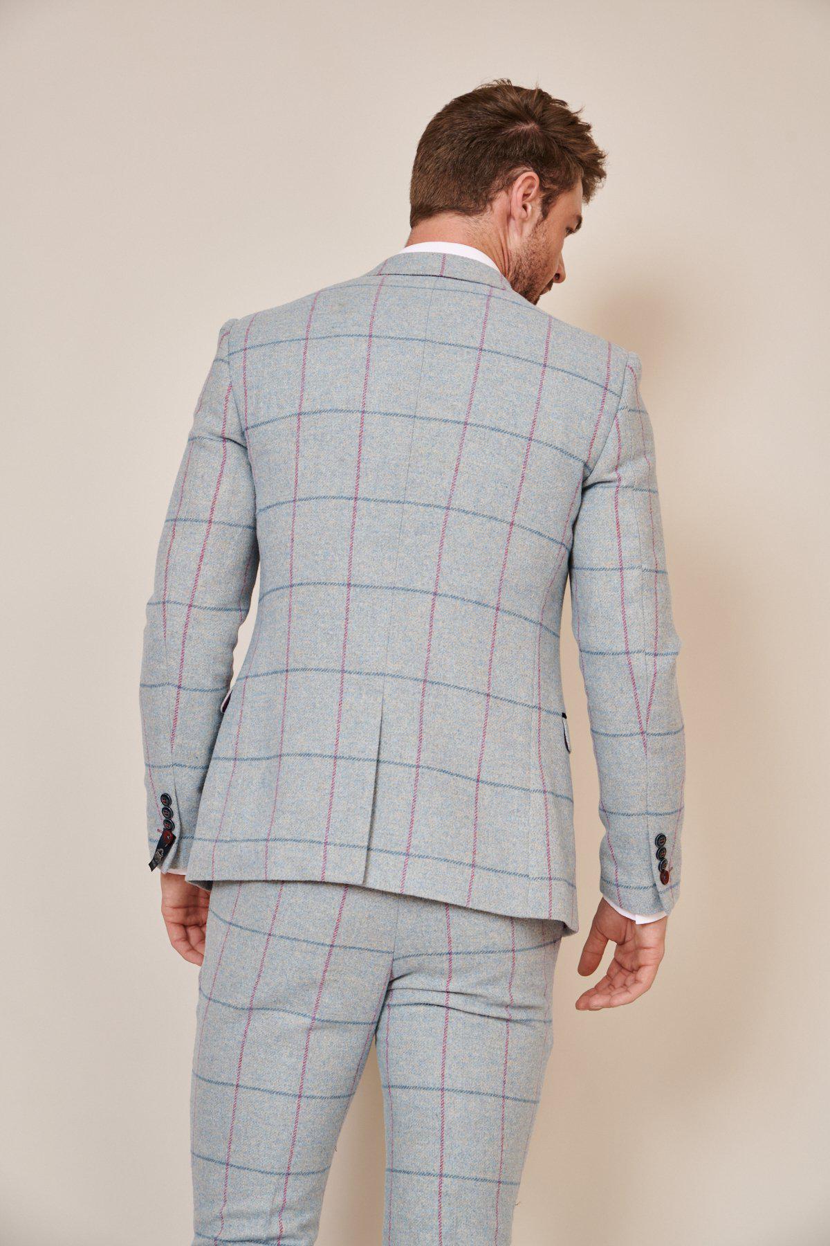 A man with light brown hair, seen from behind, wears the Marc Darcy NICOLAS - Sky Check Tweed Blazer in a slim fit; its red and blue windowpane pattern stands out against a plain beige background.