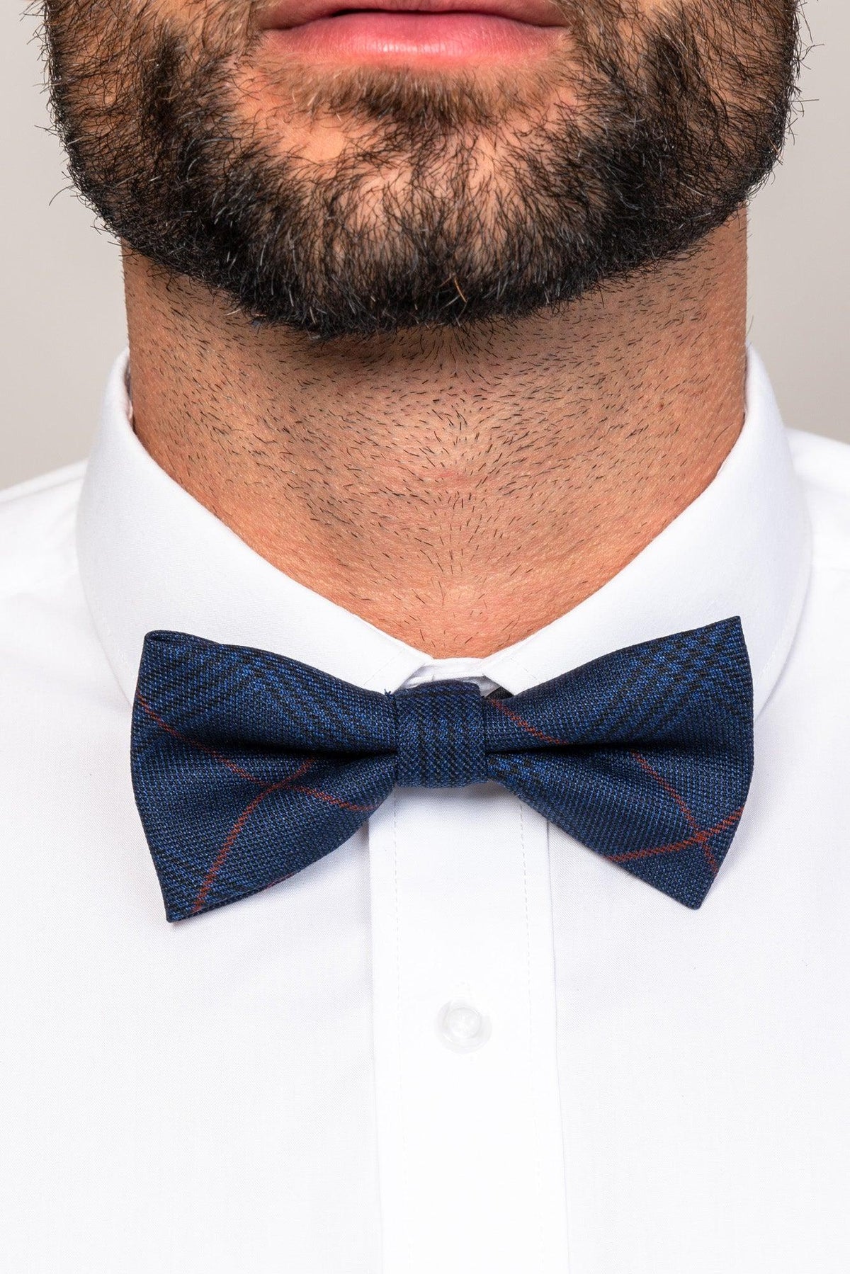 A man wearing a white dress shirt and the EDINSON - Navy Wine Check Bow Tie by Accessory, featuring a stylish navy blue plaid pattern with subtle red accents.
