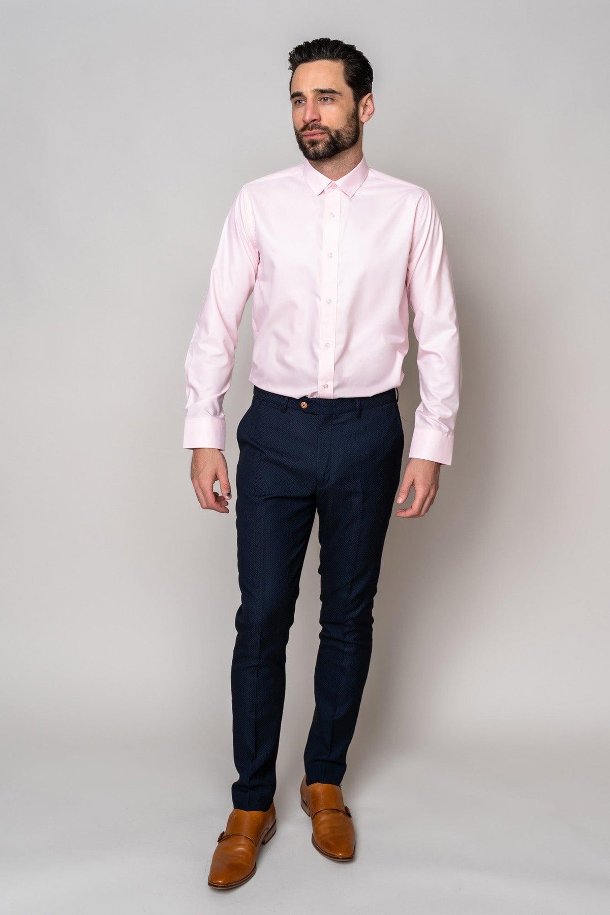 Man in Marc Darcy’s CARTER Pink Long Sleeve Shirt, paired with navy pinstripe pants and brown leather shoes, stands against a light grey background—a refined formalwear choice.