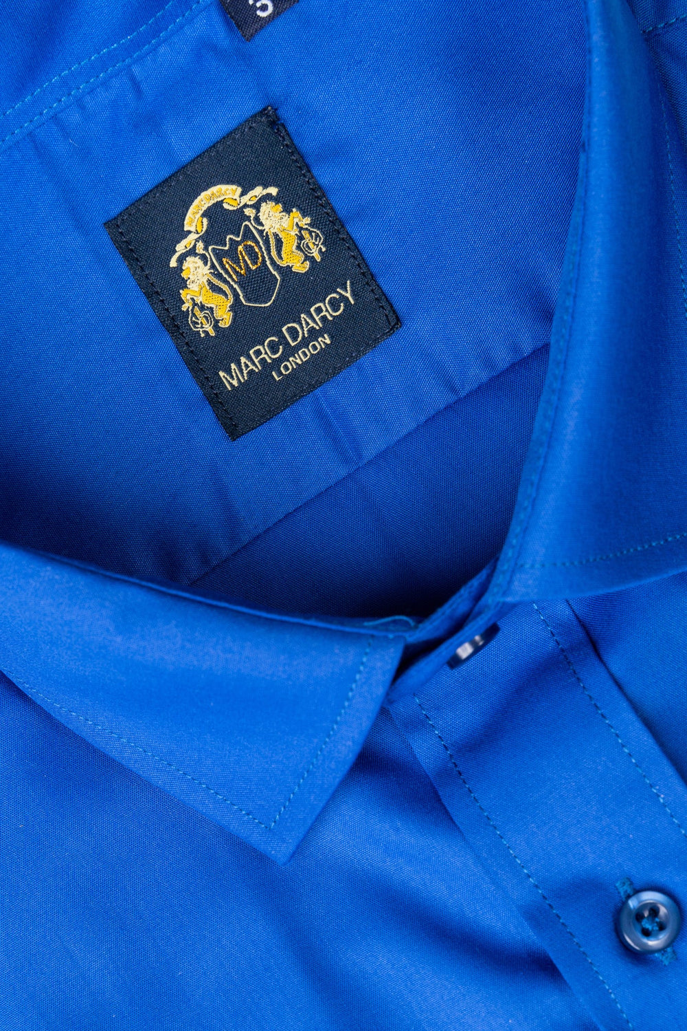 Close-up of the CARTER - Royal Long Sleeve Shirt by Marc Darcy, focusing on the collar, top button, and a black label featuring a gold crest and Marc Darcy branding.