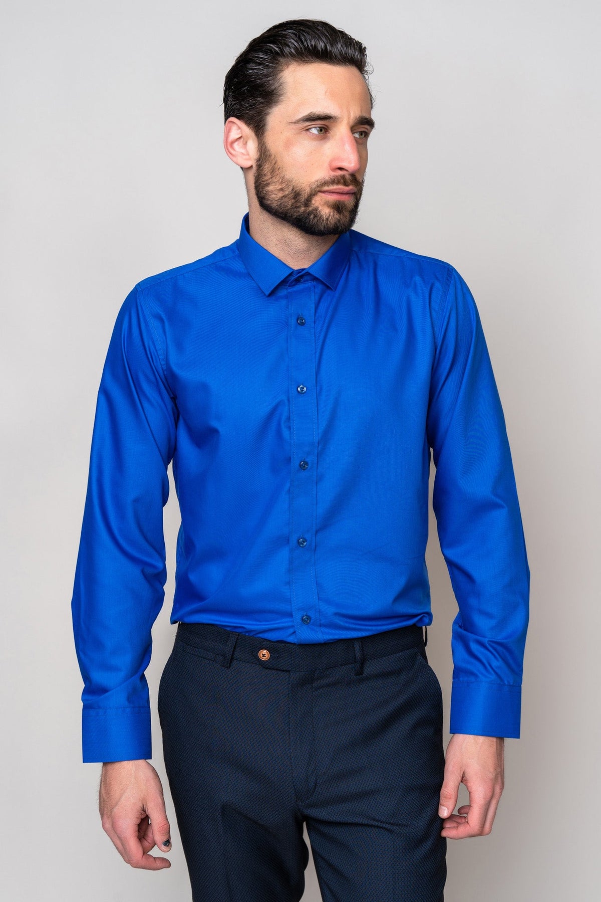 A man with dark hair and a beard is wearing the Marc Darcy CARTER Royal Long Sleeve Shirt and dark trousers, standing against a plain light gray background, looking slightly to his left.
