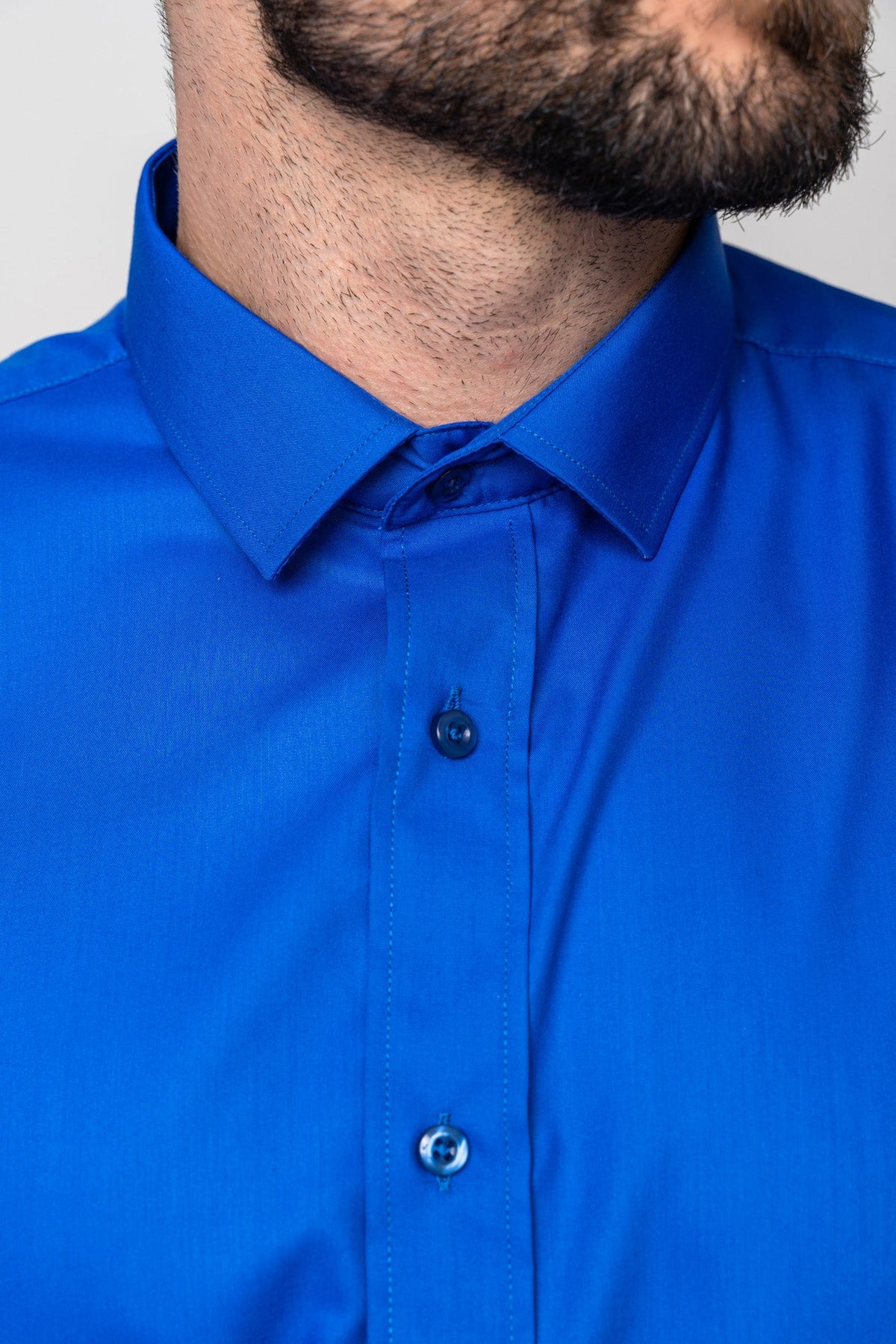 Close-up of a man in the CARTER - Royal Long Sleeve Shirt by Marc Darcy. The royal blue, classic fit shirt shows its collar, buttons, and part of his neck and short beard, with his face partially out of frame.