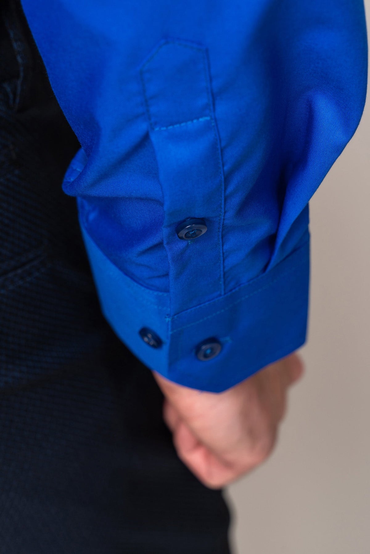 A close-up of a person’s arm wearing the CARTER - Royal Long Sleeve Shirt by Marc Darcy with buttoned cuffs and dark textured pants, showing part of the hand and detailed fabric.