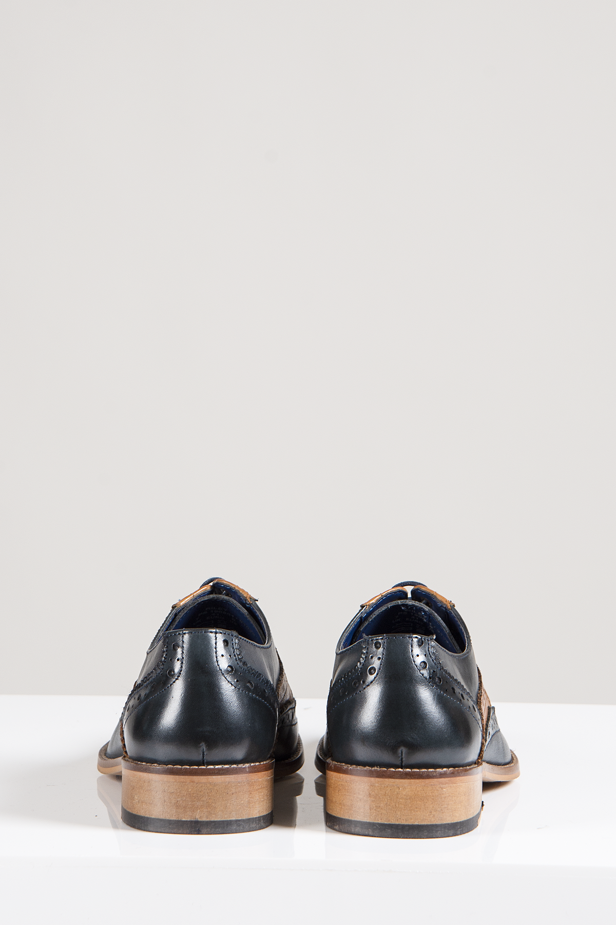The Marc Darcy RILEY Navy Tan Leather Contrast Oxford Brogue Shoes are shown from the back, displayed on a white surface with a plain light gray background.