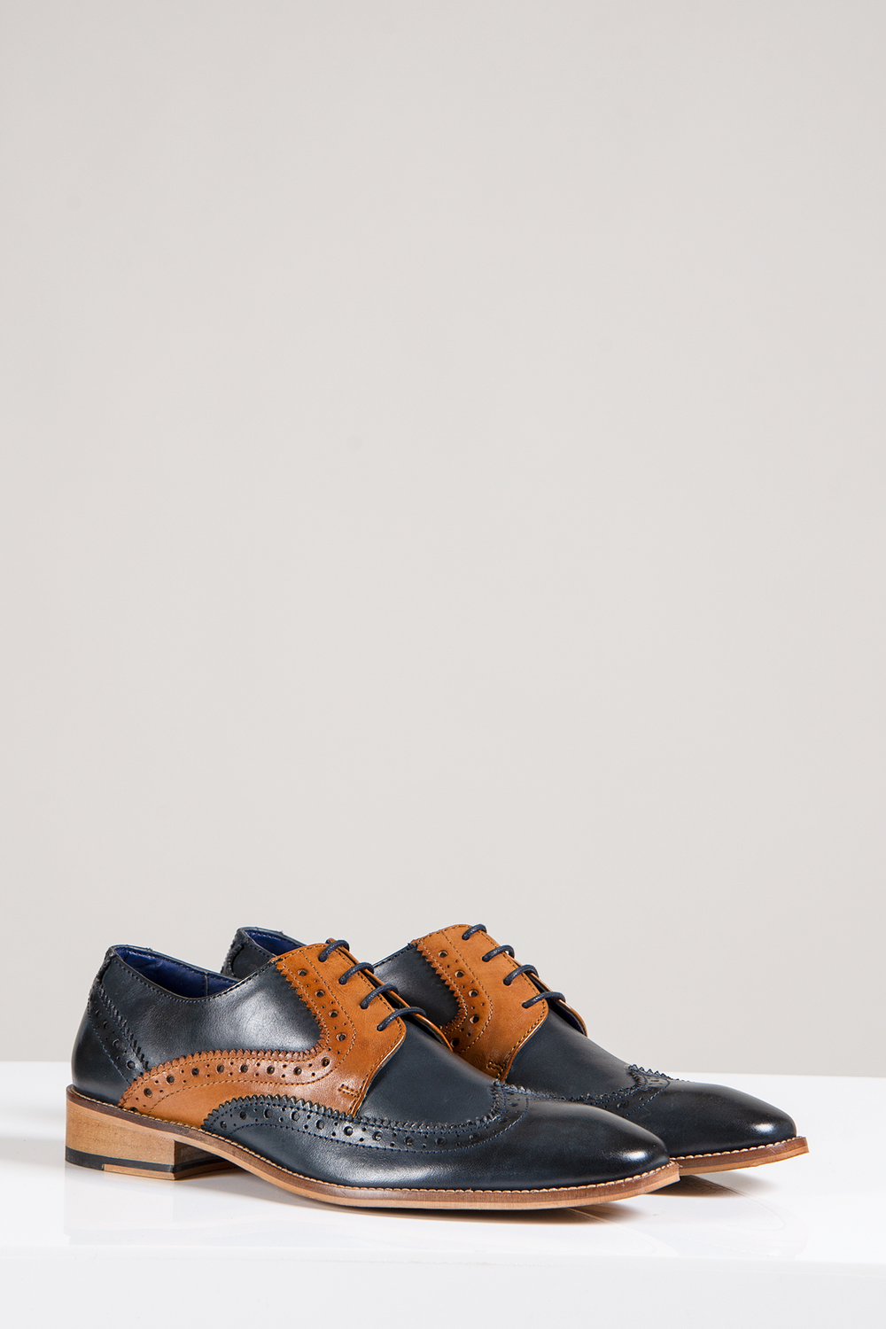 The Marc Darcy RILEY Oxford Brogue shoes feature navy and tan leather with contrast detailing, decorative perforations, and laces. Stylishly displayed on a white surface against a plain background.