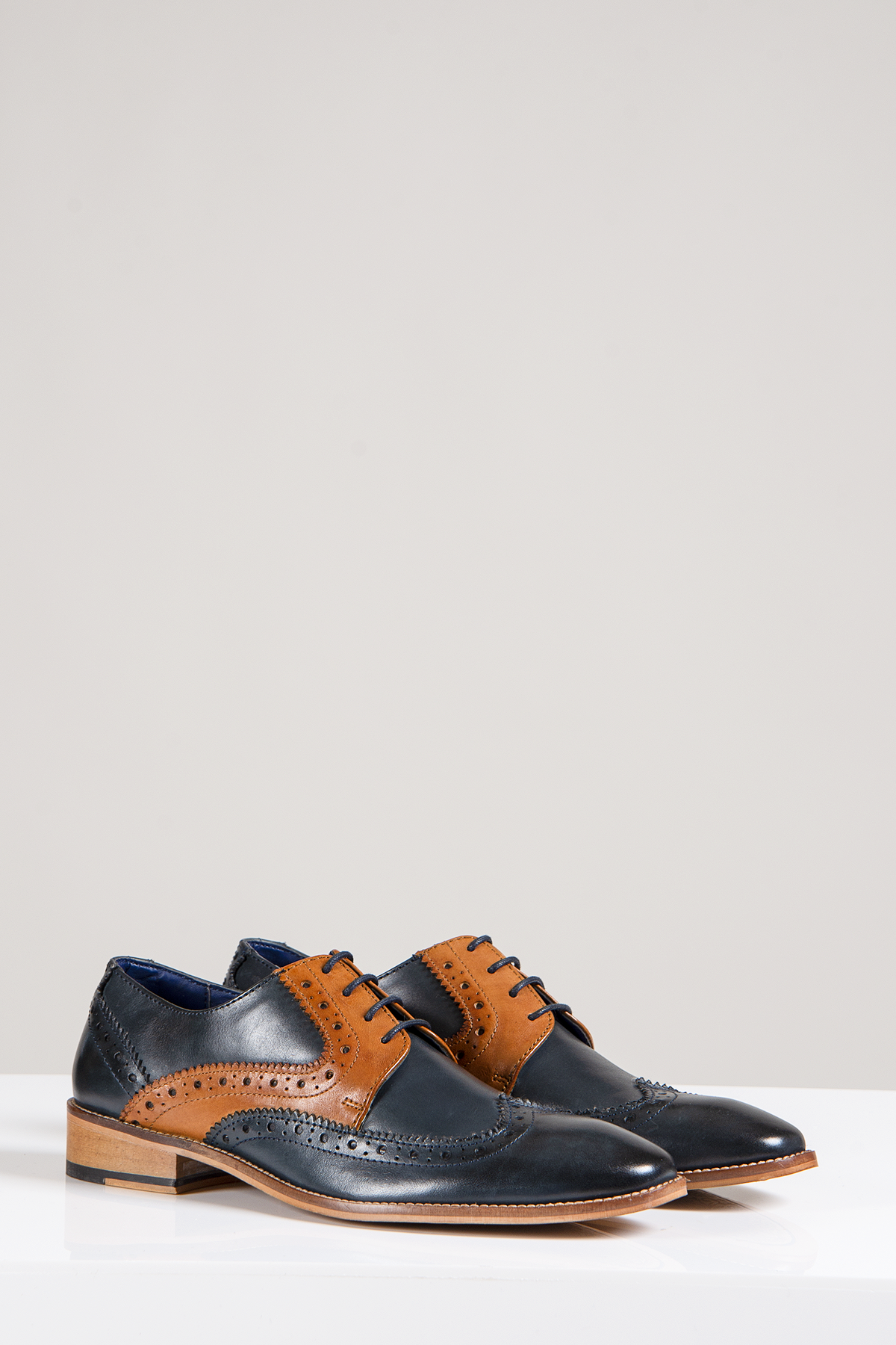 The Marc Darcy RILEY Oxford Brogue shoes feature navy and tan leather with contrast detailing, decorative perforations, and laces. Stylishly displayed on a white surface against a plain background.