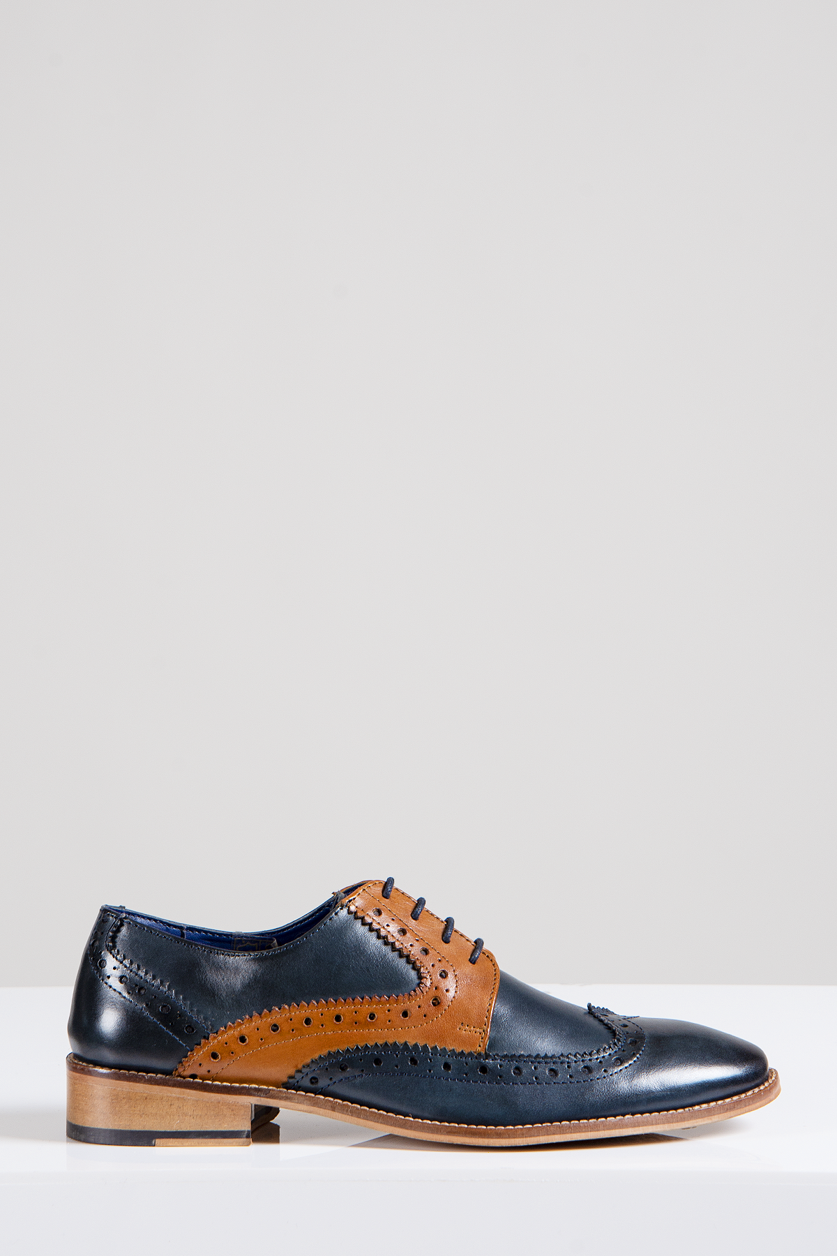 The Marc Darcy RILEY is a stylish men's oxford brogue shoe in navy and tan leather with contrast brogue detailing and black laces, shown on a white surface against a light gray background.