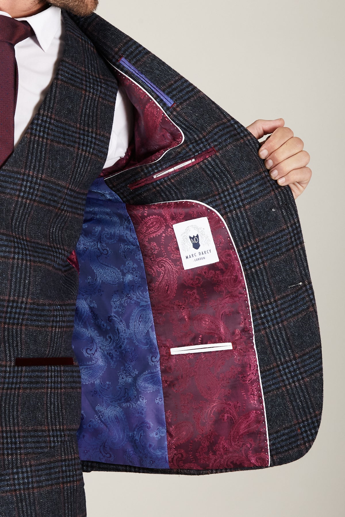 A person holds open the marcdarcy LUCA - Navy Check Tweed Blazer, revealing its vibrant blue and burgundy paisley lining and visible white label—an ideal choice for vintage style lovers.