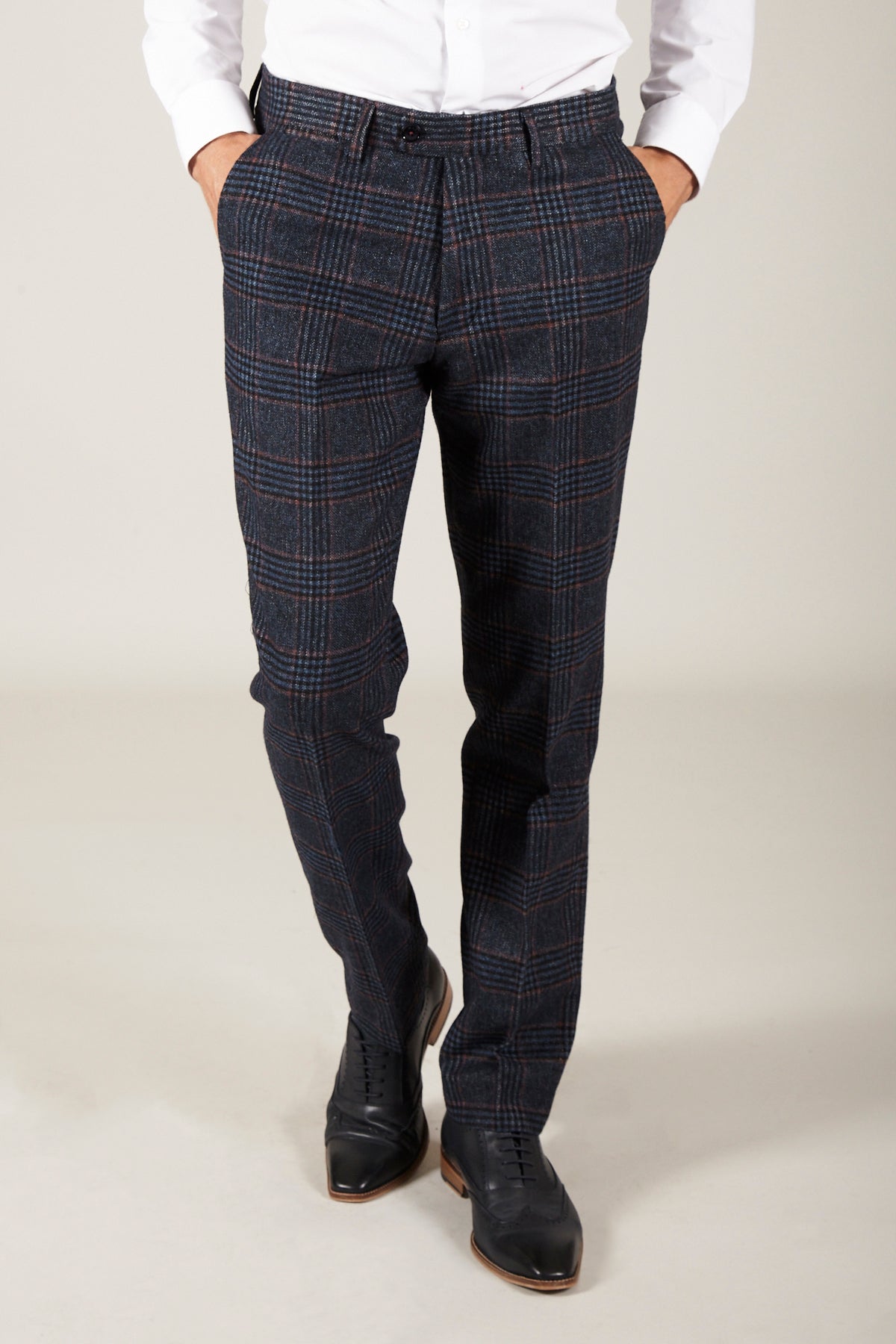 A person stands against a plain light background wearing a white dress shirt, black dress shoes, and marcdarcy's LUCA - Navy Check Tweed Trousers with hands in pockets.