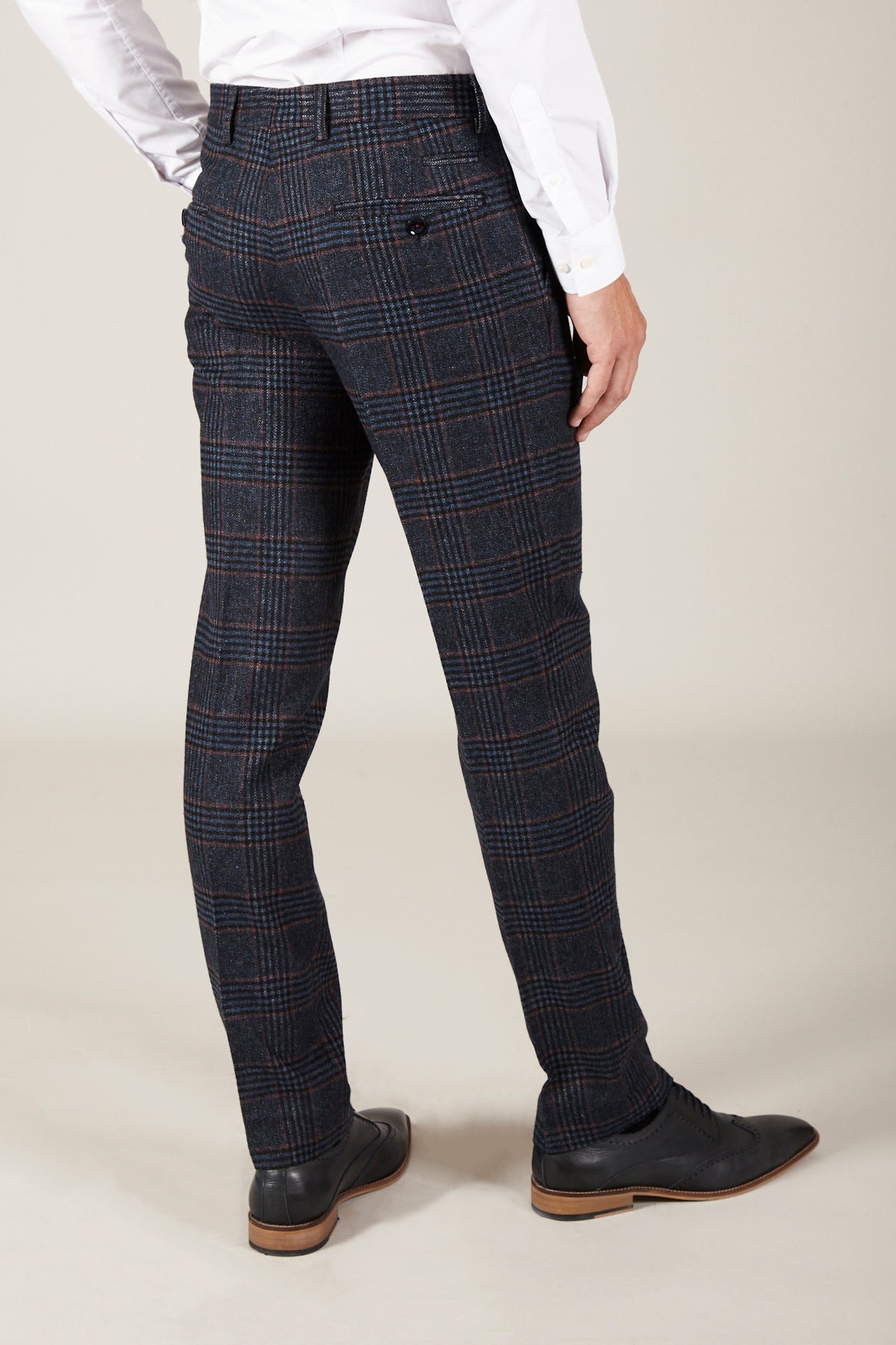 A person wearing marcdarcy LUCA - Navy Check Tweed Trousers, a white long-sleeve shirt, and black dress shoes is standing on a light-colored floor, facing away from the camera.