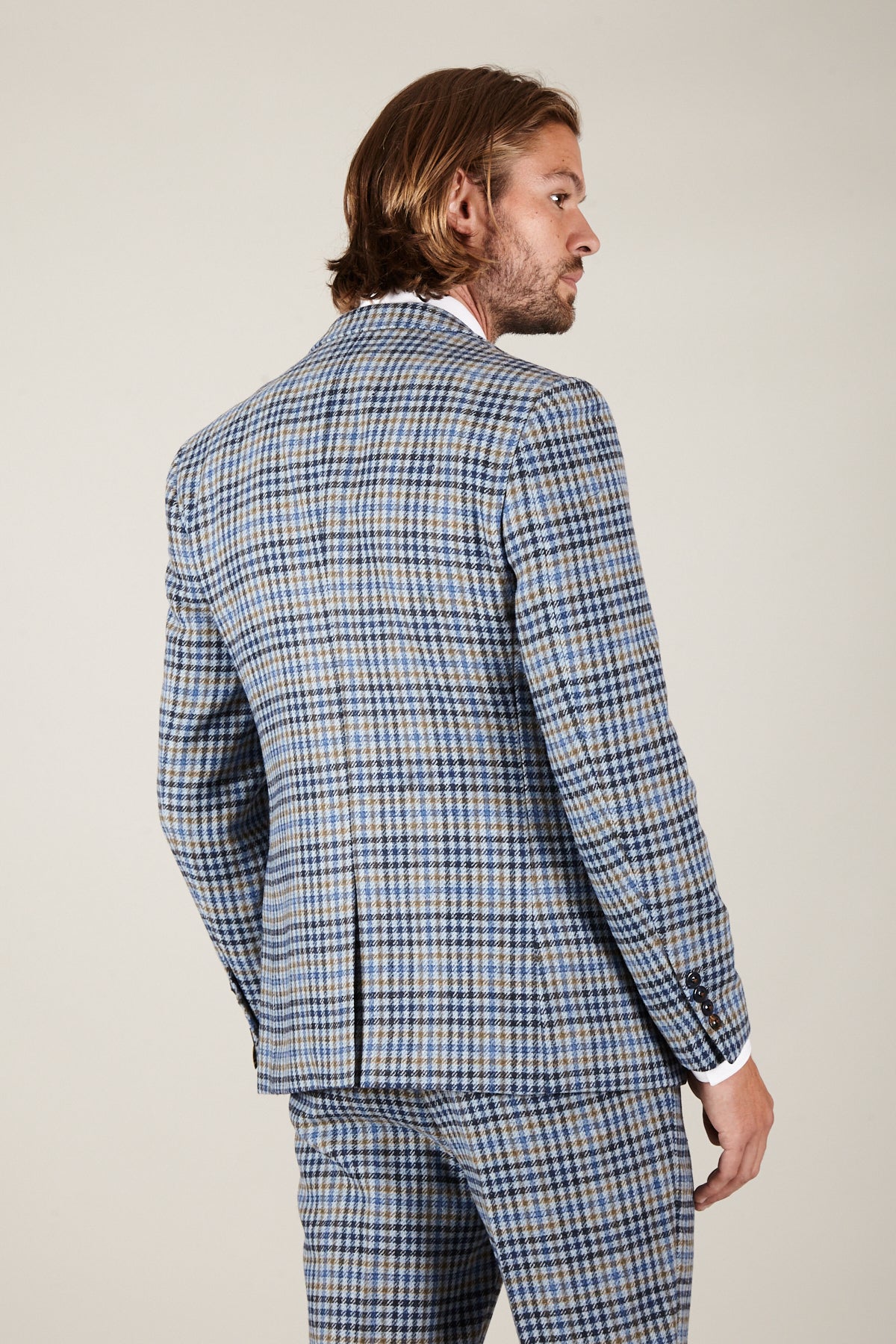 A man with medium-length hair is seen from behind wearing the Marc Darcy WATSON Blue Tan Tweed Check Blazer with matching pants and a white dress shirt, set against a plain light background.