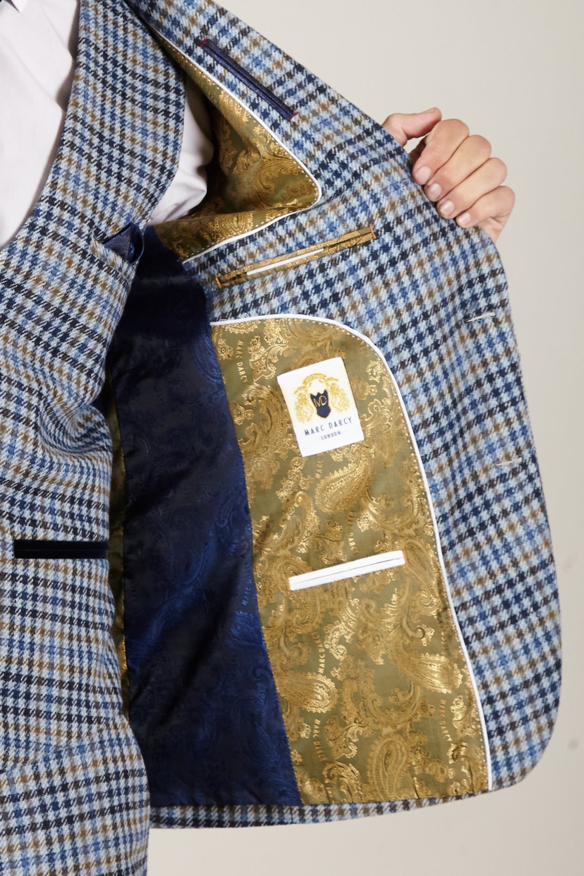 Someone displays the inside of the Marc Darcy WATSON - Blue Tan Tweed Check Blazer, which has a gold paisley lining and a navy pocket.