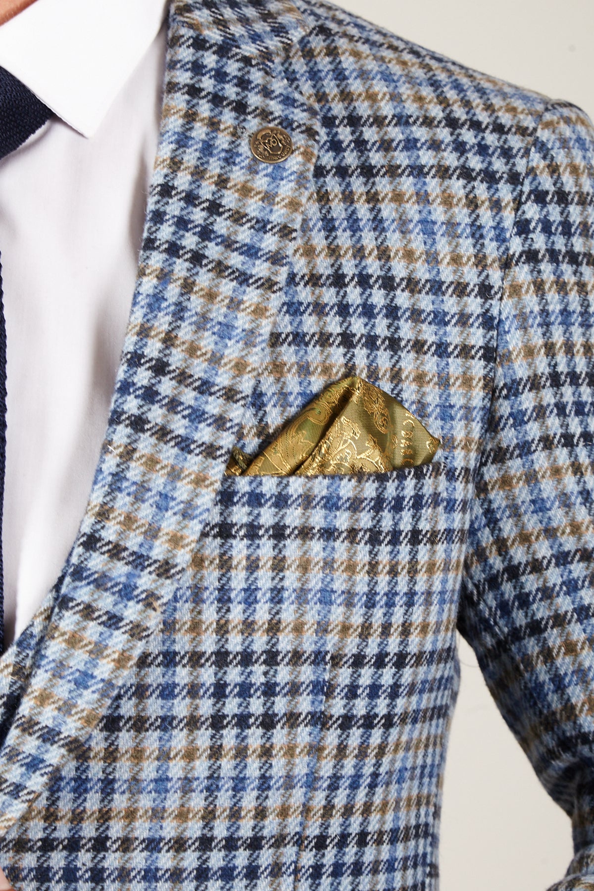 Close-up of a person in the Marc Darcy WATSON - Blue Tan Tweed Check Blazer, styled with a gold pocket square, crisp white shirt, and navy tie—a refined take on classic British suit elegance.