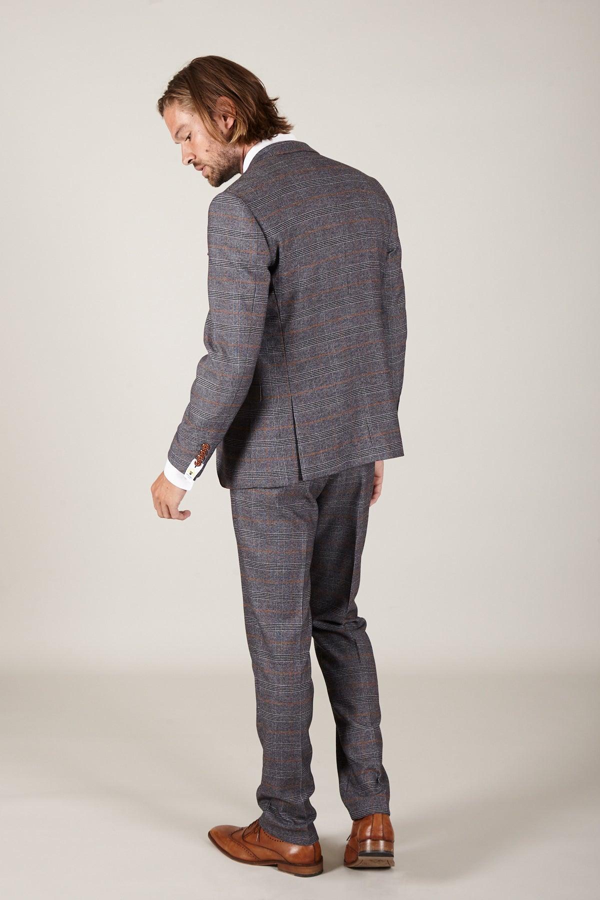 Dominic Calvert-Lewin wears the marcdarcy JENSON Grey Suit from The Everton Collection, paired with a white shirt and brown shoes, standing against a plain light background with his back slightly turned, looking down.
