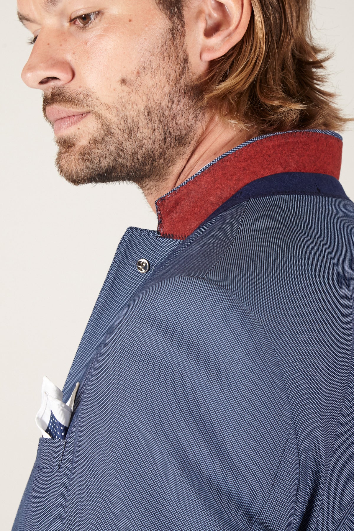 A man with light brown hair and beard wears the Marc Darcy DANNY - Sky Tailored Blazer, a slim fit blue blazer with a red and blue collar. A white pocket square with blue edging peeks from the breast pocket; his face is shown in profile.