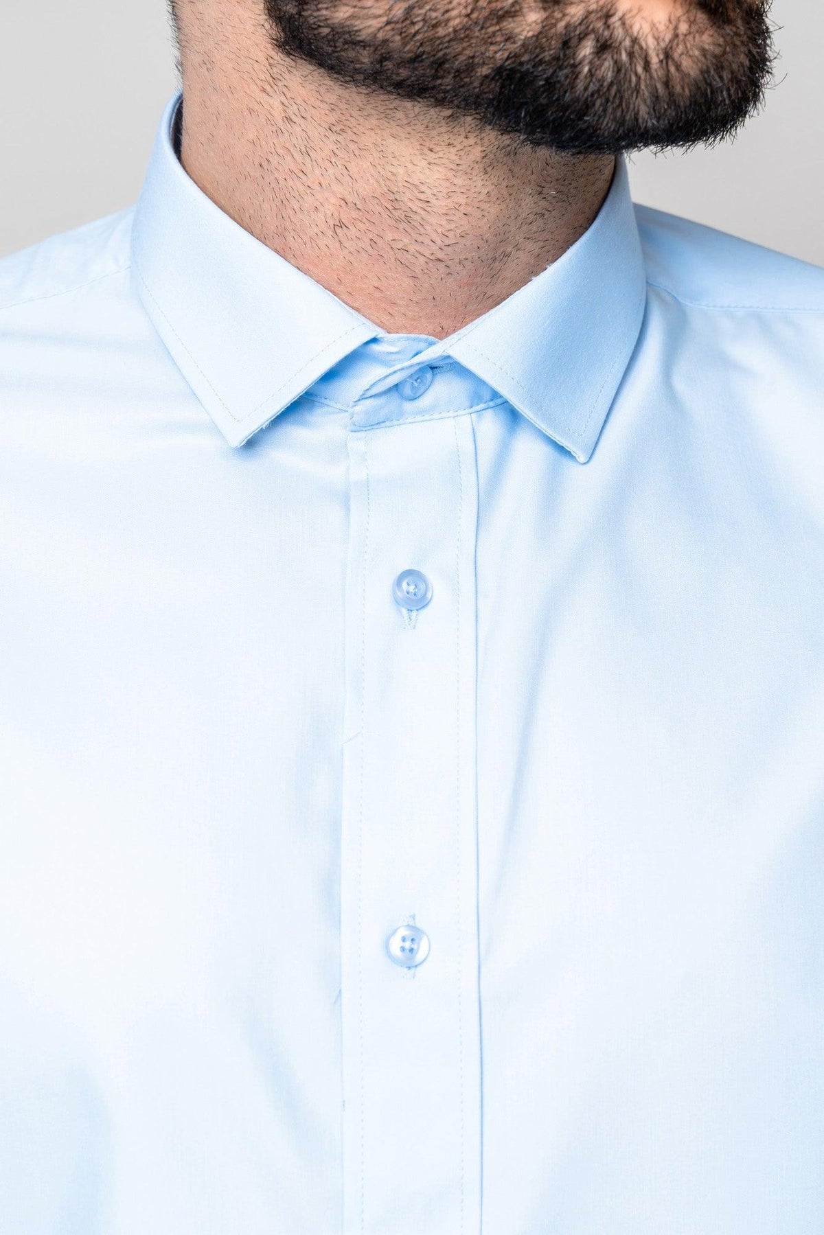 A close-up of a man wearing the Marc Darcy CARTER - Sky Long Sleeve Shirt with a spread collar, showing the buttons and part of his bearded jawline and neck. His face is slightly turned, highlighting the classic fit.
