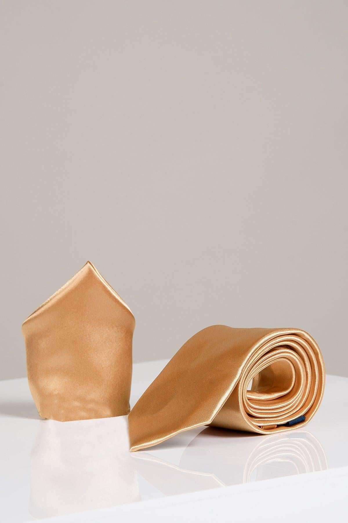 The Accessory STANLEY - Satin Tie and Pocket Square Set in Gold features a rolled gold satin tie beside a matching pocket square, elegantly displayed on a glossy white surface with a plain light gray background.
