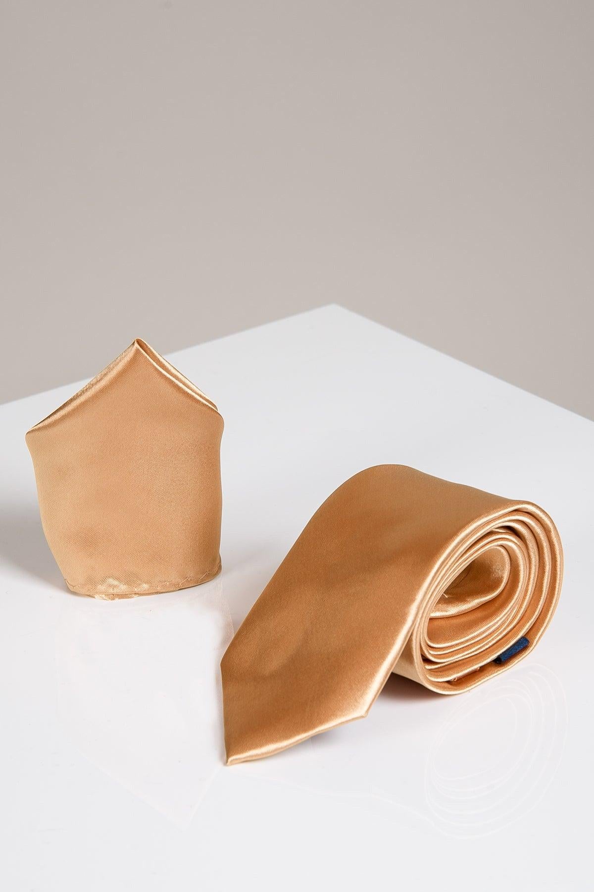 The STANLEY - Satin Tie and Pocket Square Set in Gold by Accessory features a shiny satin tie rolled up next to its matching pocket square, both displayed on a glossy white surface with a neutral backdrop.