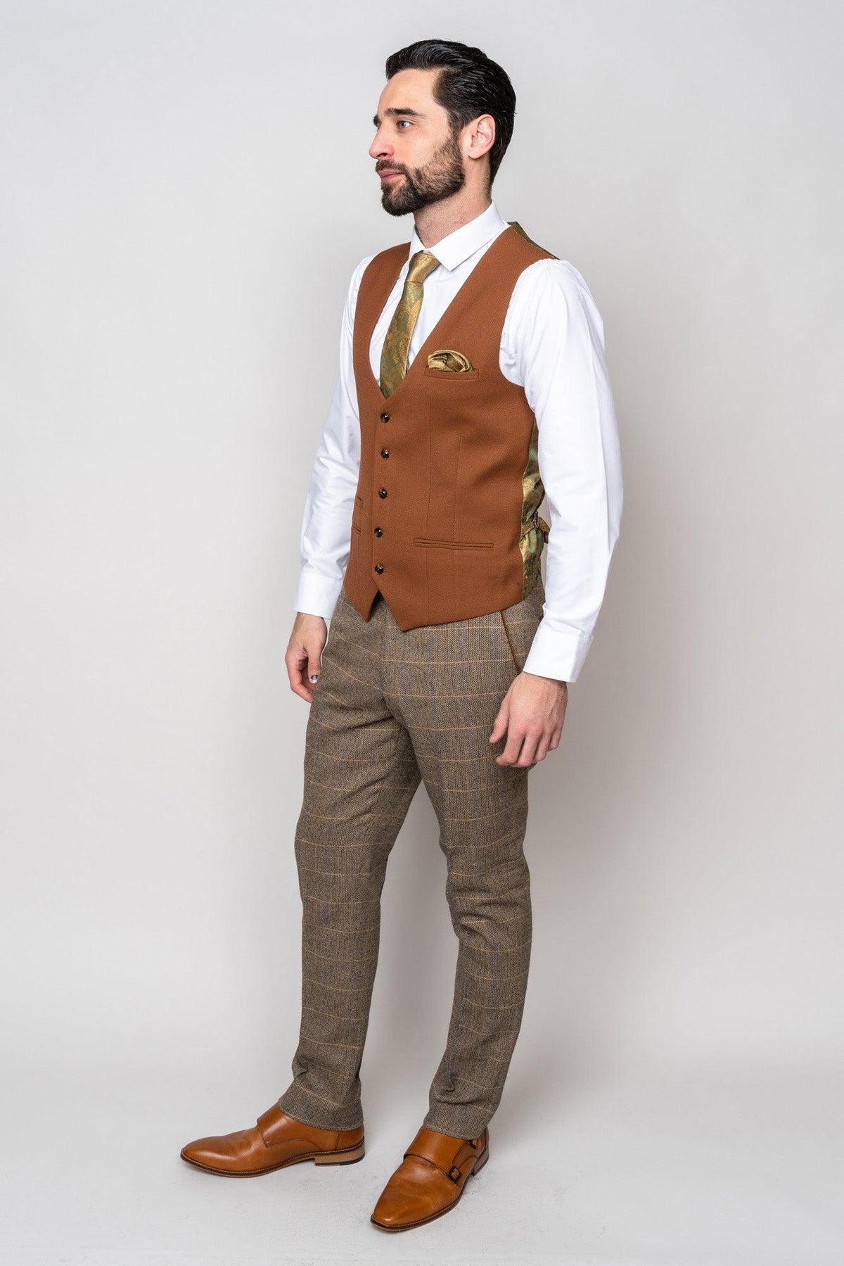 A man with dark hair and a beard wears the marcdarcy TED Tan Tweed Check Suit with Kelvin Tan Waistcoat over a white shirt, gold tie, plaid trousers, and brown shoes, standing against a plain light background.