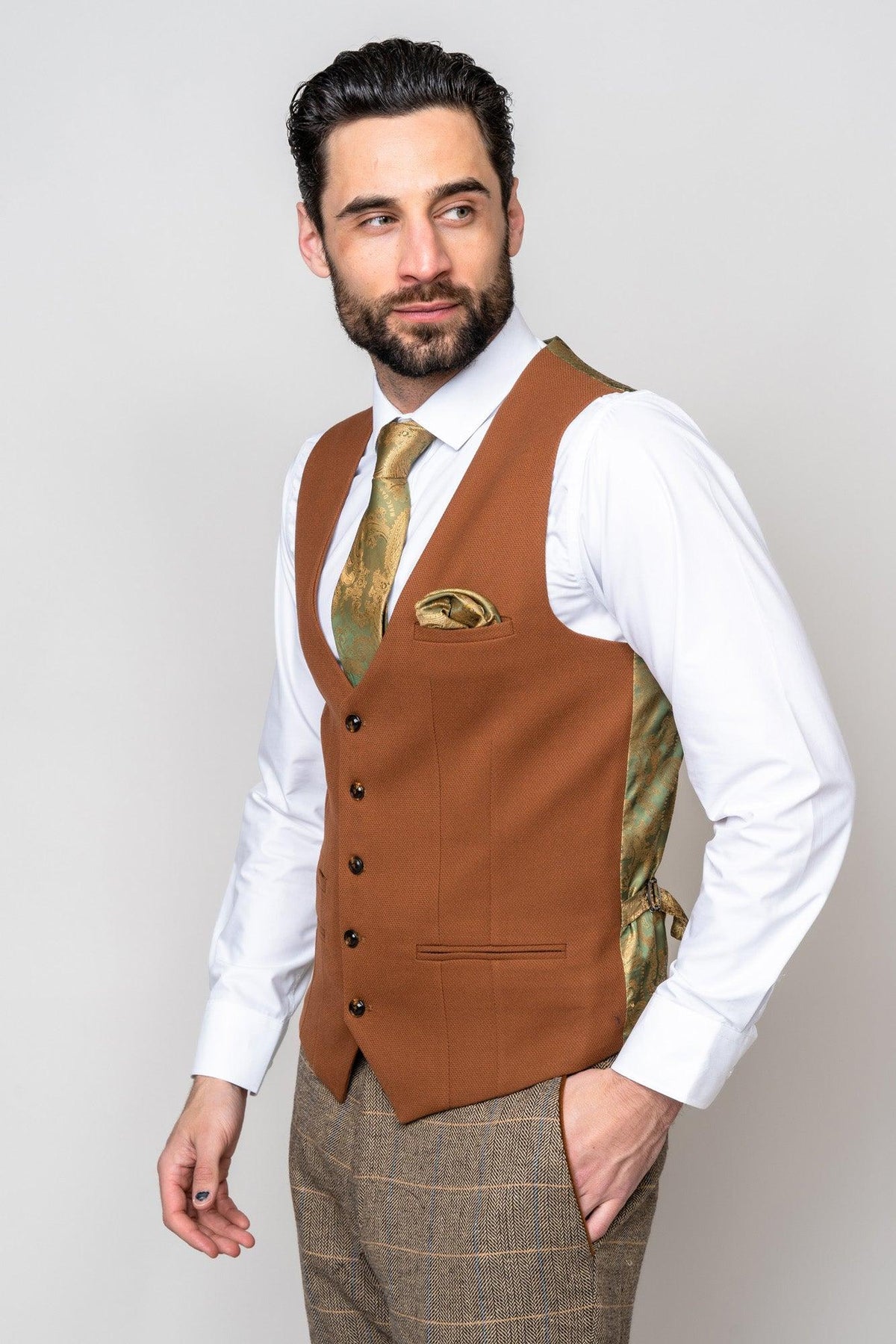 A man with dark hair and a beard wears the marcdarcy TED Tan Tweed Check Suit with Kelvin Tan Waistcoat: a white shirt, gold patterned tie, matching pocket square, and brown plaid trousers—ideal for a stylish country barn wedding.