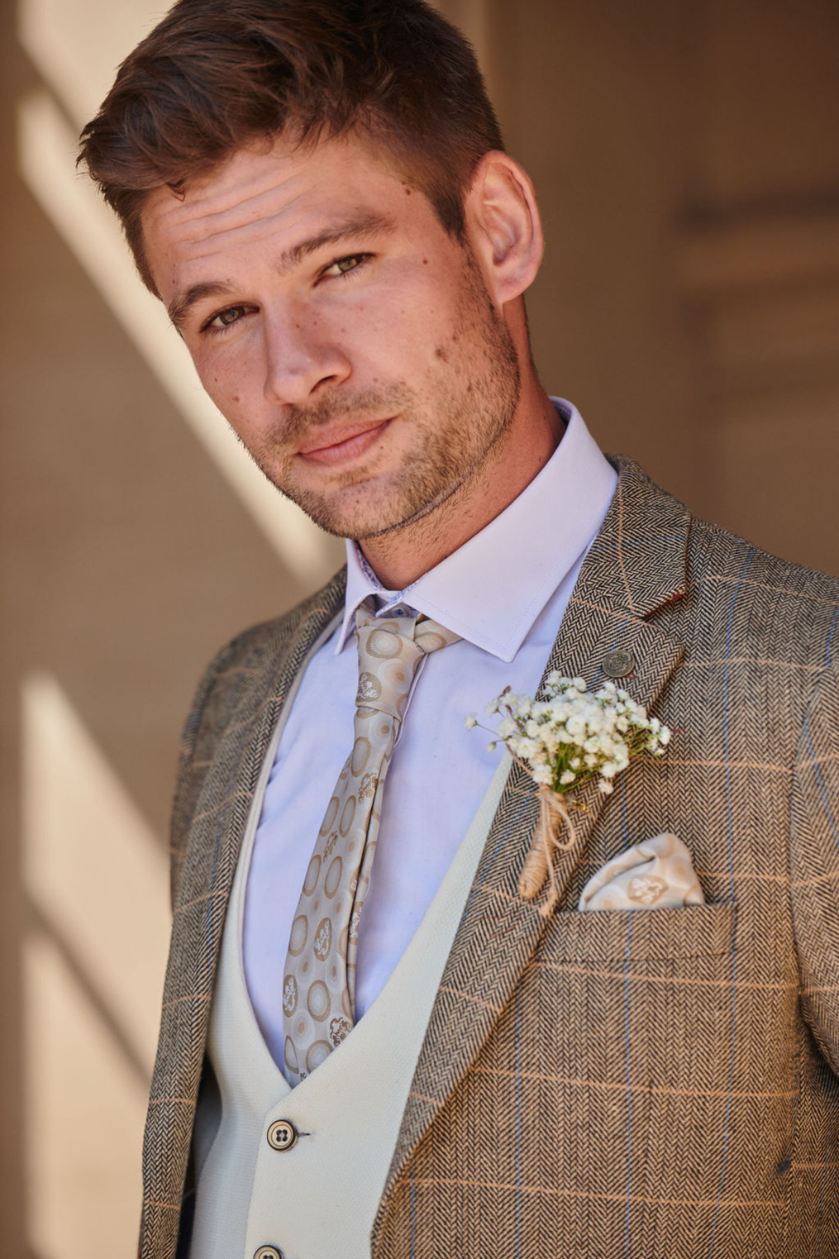 Groom wears the marcdarcy TED Tan Tweed Check Suit with a Kelvin Cream Waistcoat, paired with a patterned tie and boutonnière for a vintage-inspired look.