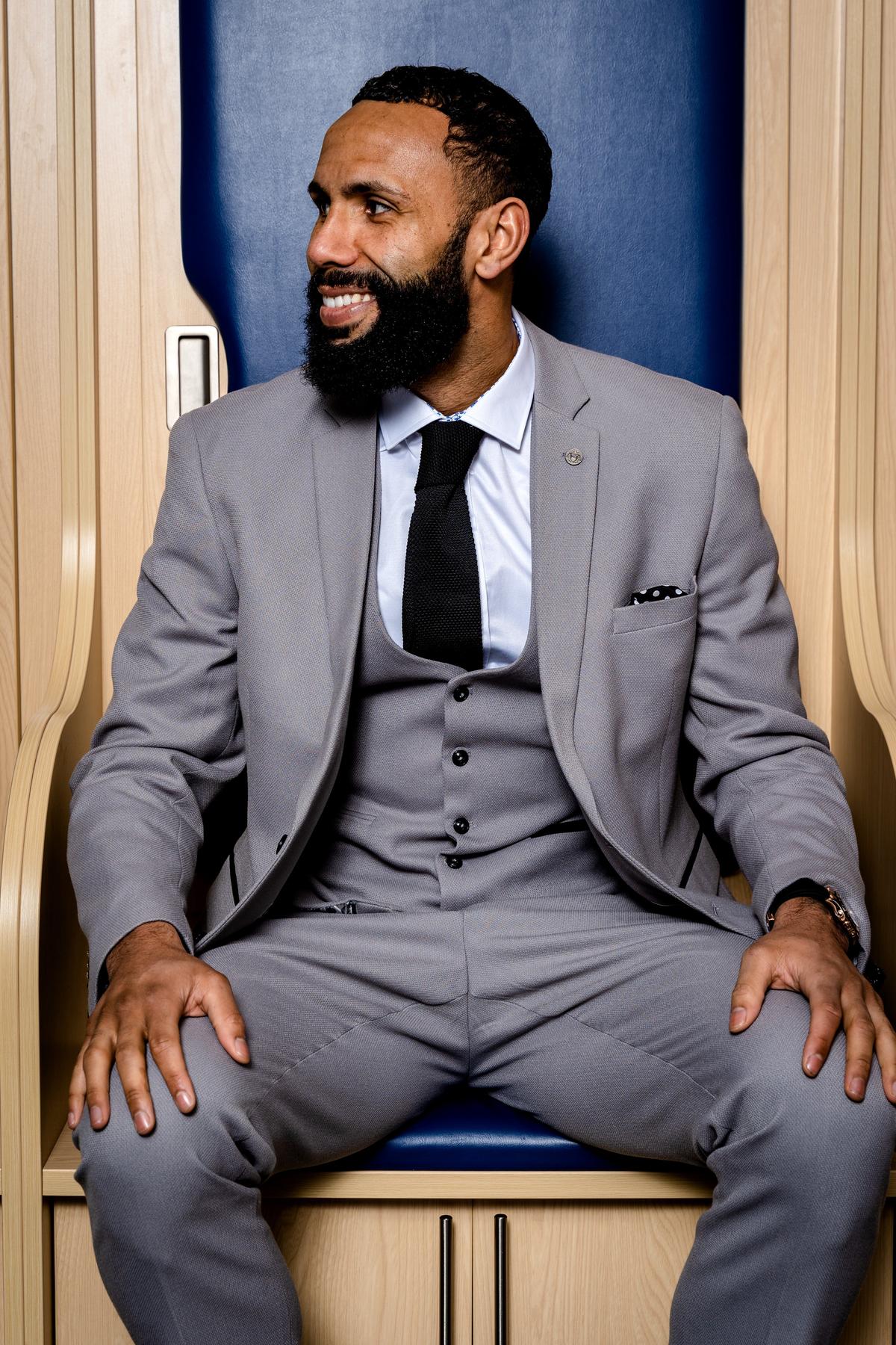 A man with a beard smiles in a locker room, wearing the marcdarcy Edwin Suit from The WBA Collection, as worn by Kyle Bartley.