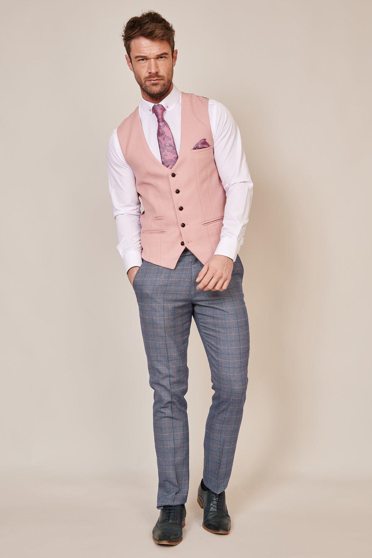 A man with short hair and a beard faces the camera, wearing the marcdarcy KELVIN Pink Single Breasted Waistcoat over a white shirt, a paisley accessory set, blue plaid trousers, and dark shoes against a plain background.