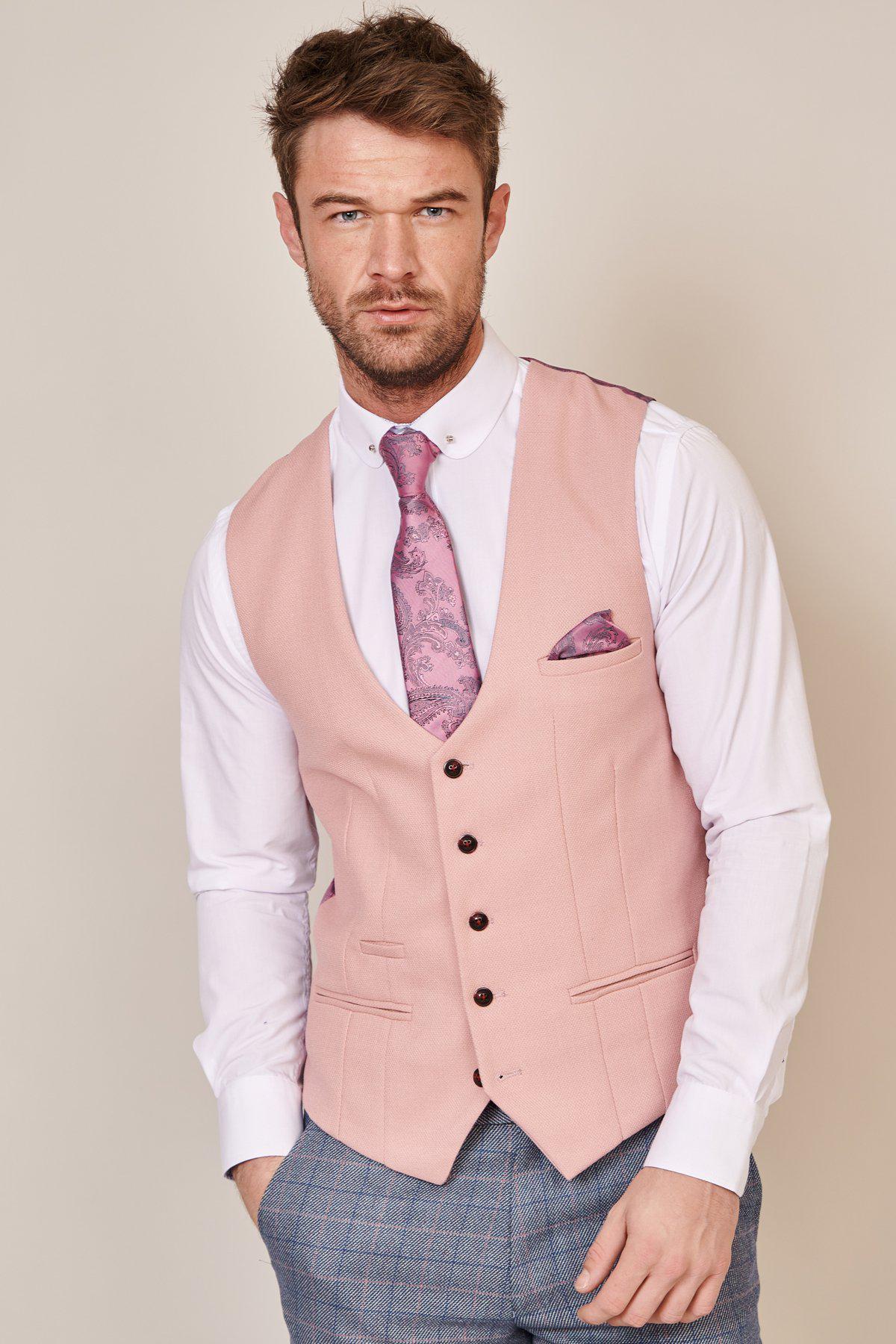 A man models the marcdarcy KELVIN Pink Single Breasted Waistcoat over a white shirt with a lavender tie and pocket square, paired with blue plaid trousers, against a neutral background.