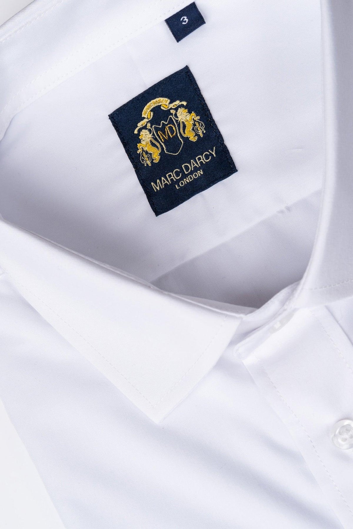 A close-up of the CARTER White Long Sleeve Shirt by Marc Darcy, featuring a classic collar, button placket, and a navy blue label with gold detailing reading "Marc Darcy London" sewn inside the collar.