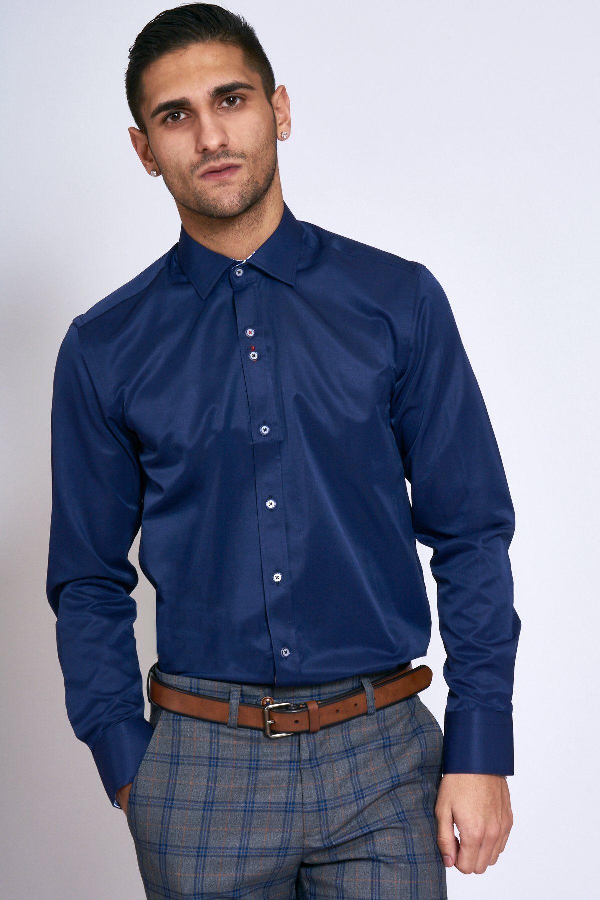 A man wearing the Marc Darcy ALFIE navy long sleeve shirt and plaid gray trousers with a brown belt stands against a plain light background, looking at the camera with a neutral expression.