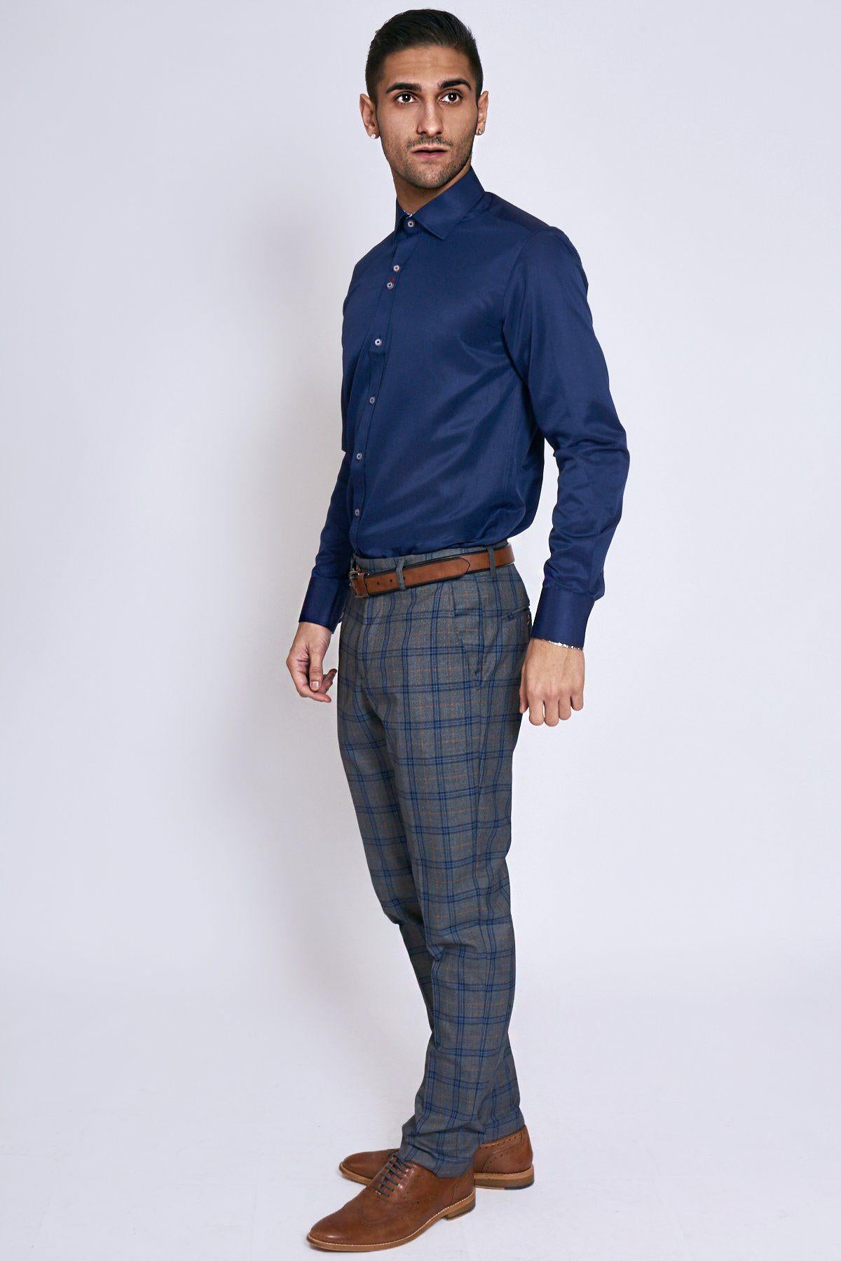A man stands against a plain background, wearing the Marc Darcy ALFIE Navy Long Sleeve Shirt, paired with plaid trousers, a brown belt, and brown dress shoes. He looks slightly to the side with a neutral expression.