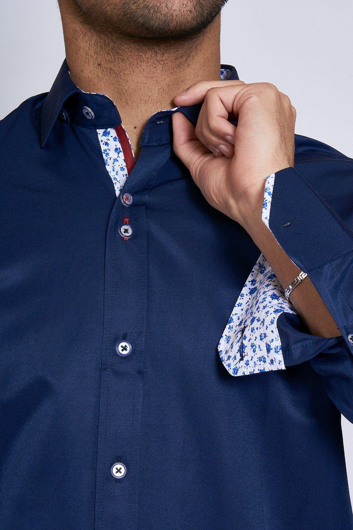 A person adjusts the collar of a Marc Darcy ALFIE Navy Long Sleeve Shirt, revealing floral-patterned inner cuffs and collar. Only the lower face and upper torso are visible.