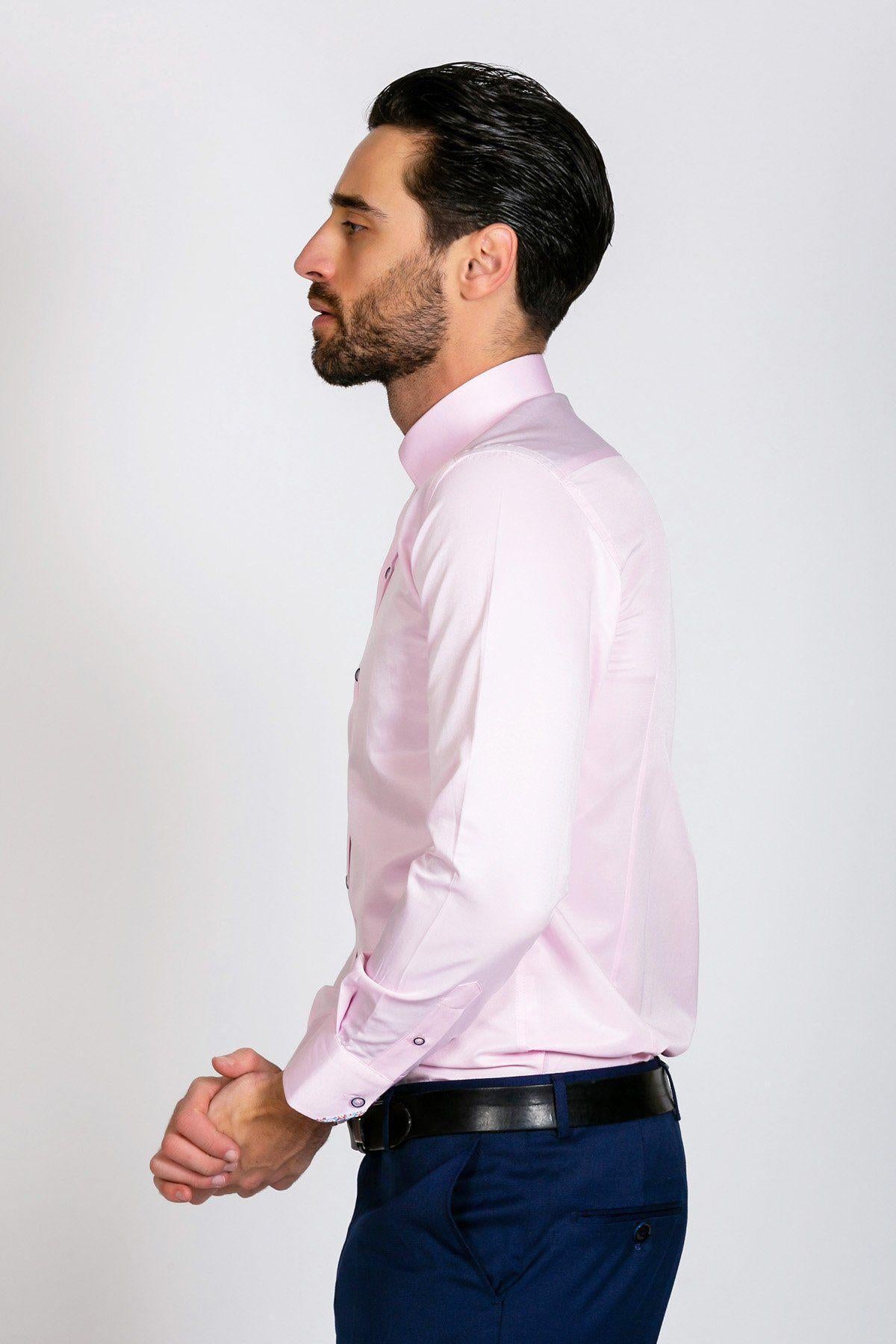 A man with short dark hair and a beard stands in profile, wearing the Marc Darcy ALFIE Pink Long Sleeve Shirt in a classic fit, tucked into navy blue trousers with a black belt. His hands are loosely clasped in front of him against a plain background.