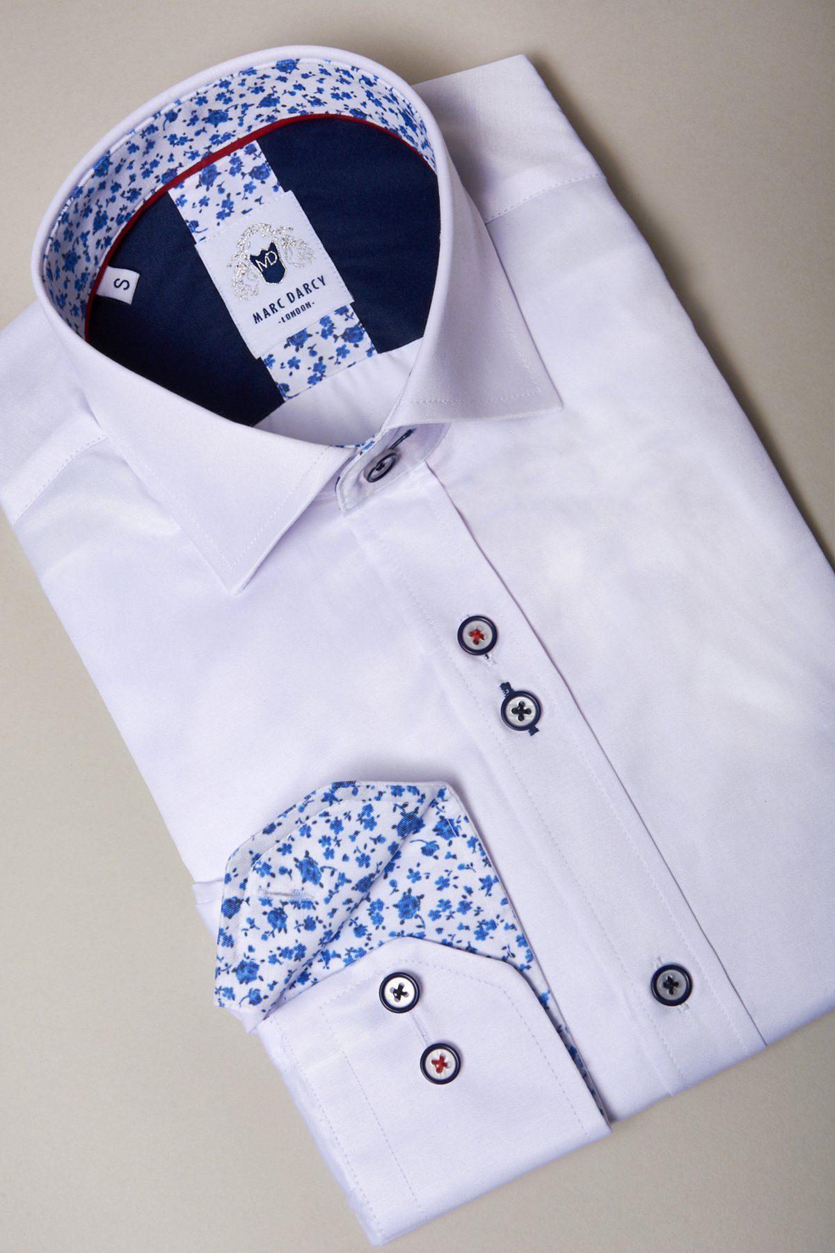 The ALFIE White Long Sleeve Shirt by Marc Darcy is crafted from a cotton blend, with blue and white floral inner collar and cuffs, black buttons with red accents, and a label inside the collar. It’s shown folded on a neutral background.
