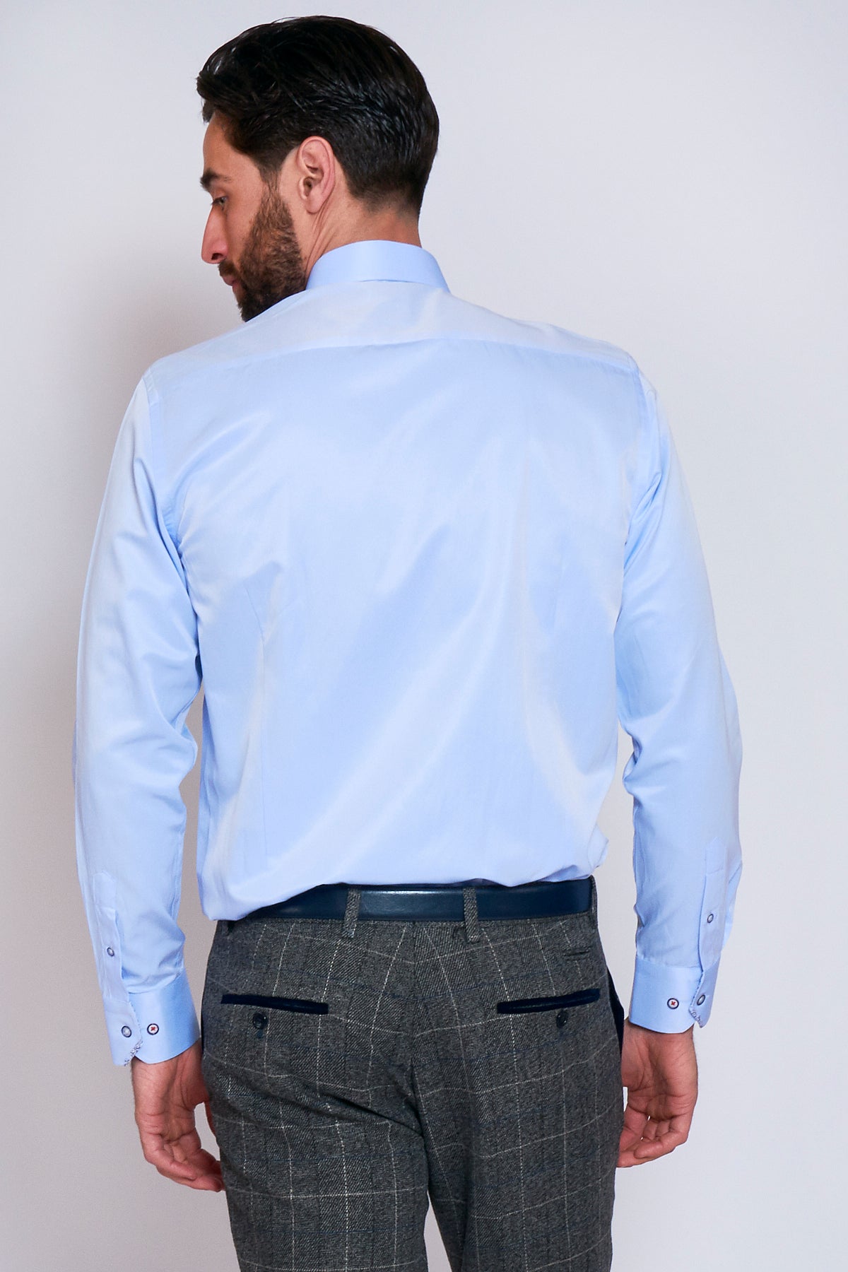 A man with dark hair and a beard is seen from behind wearing the Marc Darcy ALFIE Sky Blue Long Sleeve Shirt in a classic fit, paired with gray plaid dress pants and a dark belt, against a plain light background.