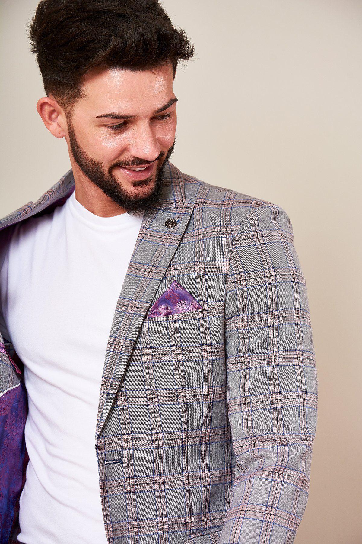 A man with dark hair and a beard smiles while looking down, wearing the Marc Darcy ALVIN - Grey Pink Check Blazer with a white t-shirt underneath; the stylish lining and purple pocket square add standout details to this slim fit piece.