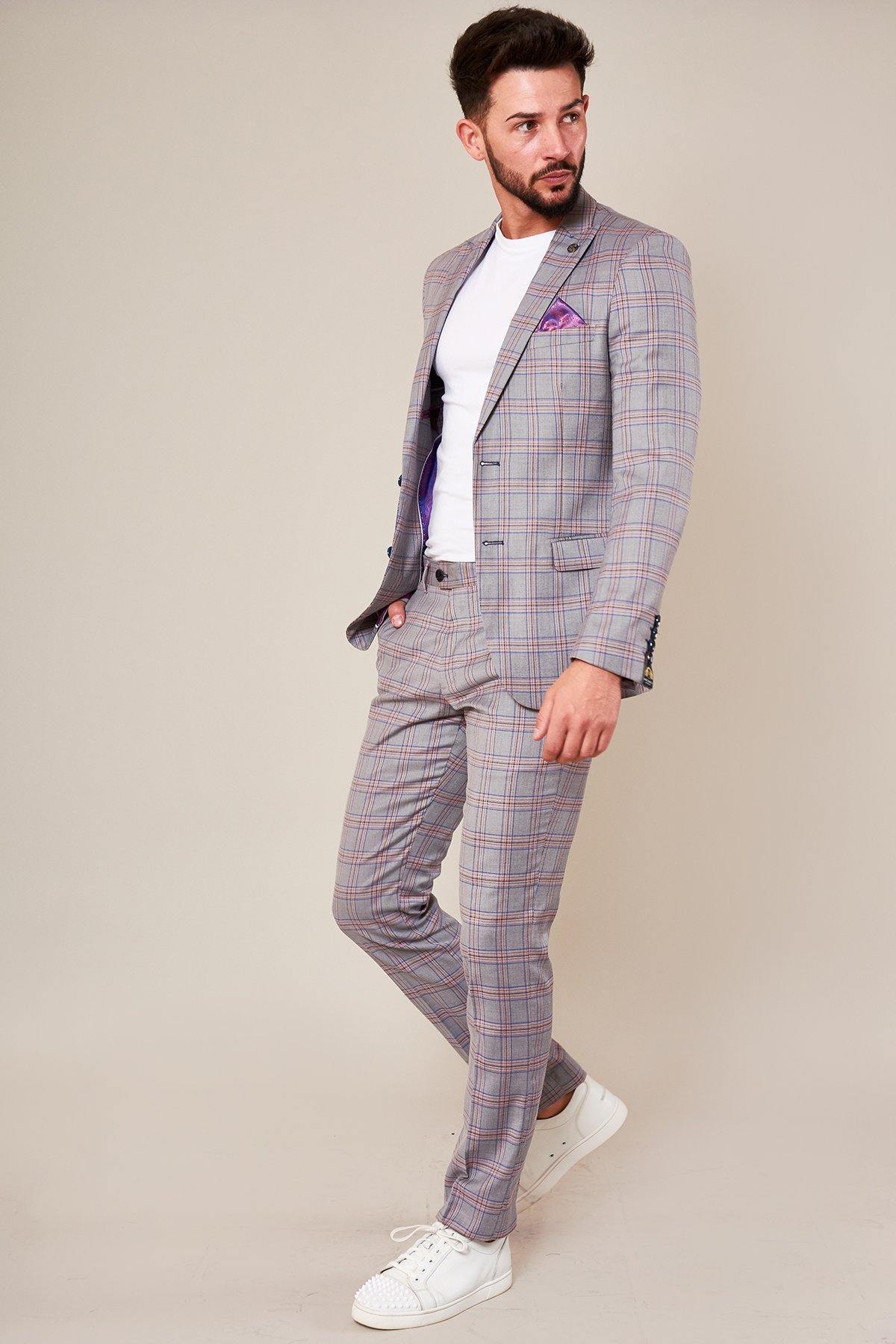 A man with dark hair and a beard wears the Marc Darcy ALVIN Grey Pink Check Blazer with a light purple pocket square, white t-shirt, and white sneakers, standing against a plain beige background.