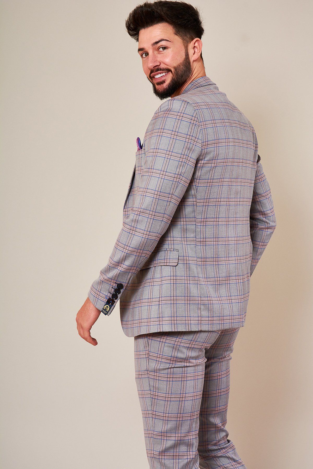 A man with short dark hair and a beard, wearing the Marc Darcy ALVIN Grey Pink Check Blazer, stands turned to the side and smiles over his shoulder against a plain background.