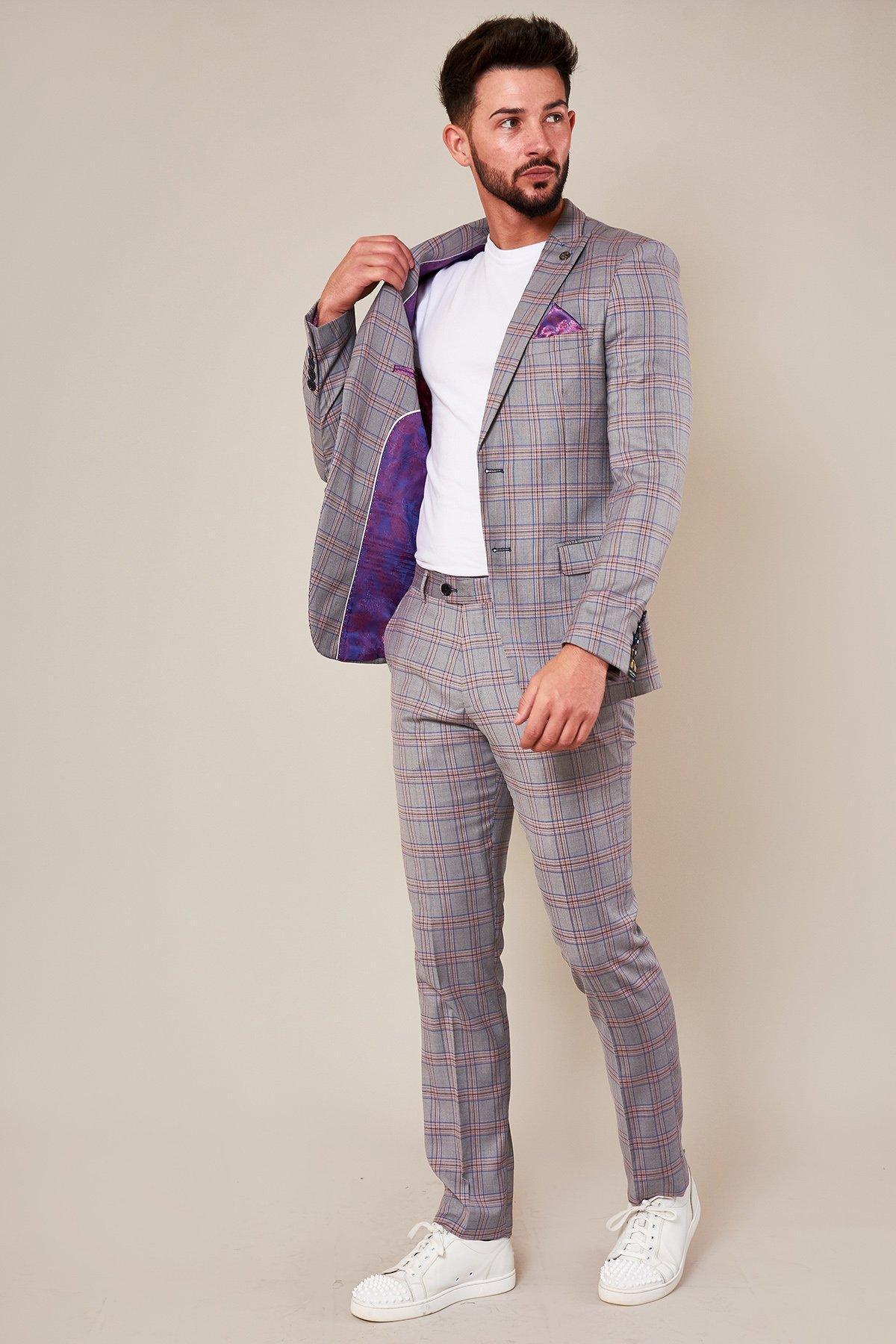 A man models the Marc Darcy ALVIN – Grey Pink Check Blazer paired with a white t-shirt and sneakers. He opens the blazer to reveal its bold purple lining, making it a standout piece against a plain beige background.