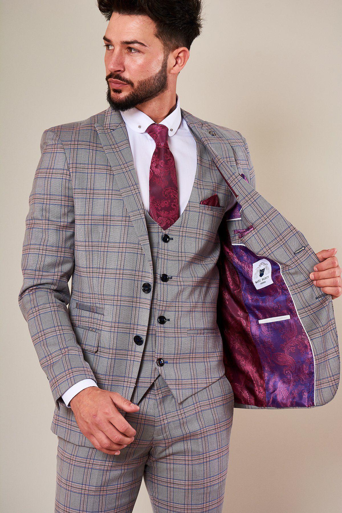 A man in a slim fit Marc Darcy ALVIN - Grey Pink Check Blazer with a white shirt and red paisley tie reveals the blazer’s vibrant purple paisley lining, making it a standout piece as he looks to his left.