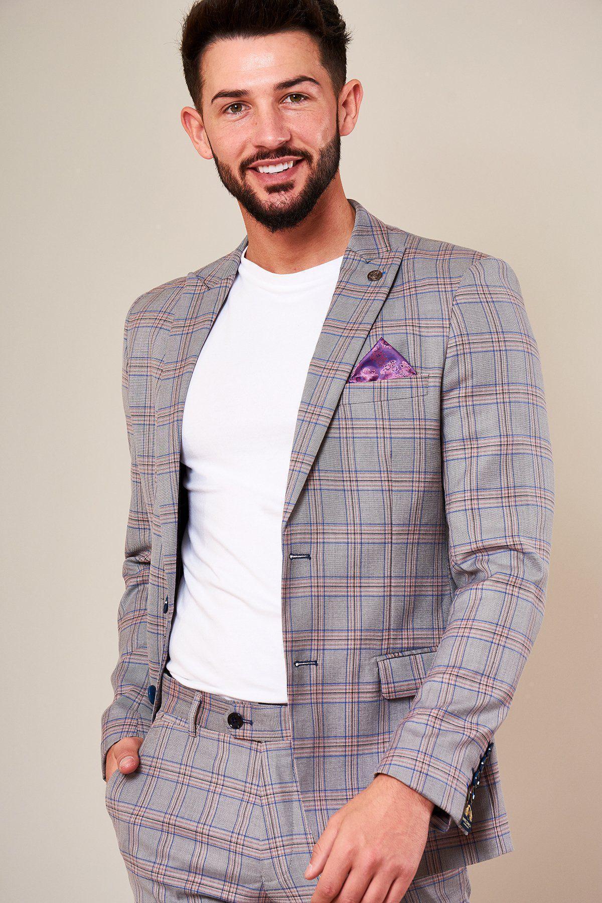 A man with short dark hair and a beard smiles, wearing the Marc Darcy ALVIN Grey Pink Check Blazer with a purple pocket square and white t-shirt, standing with one hand in his pocket against a plain background.