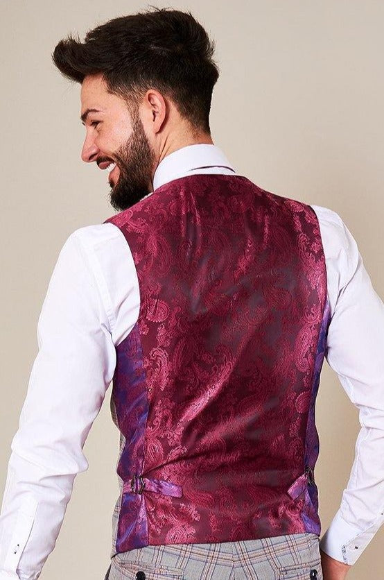A man with dark hair and a beard smiles, wearing a white shirt and the Marc Darcy ALVIN Grey Pink Check Single Breasted Waistcoat, seen from the back. He pairs it with light-colored plaid trousers for a stylish look.