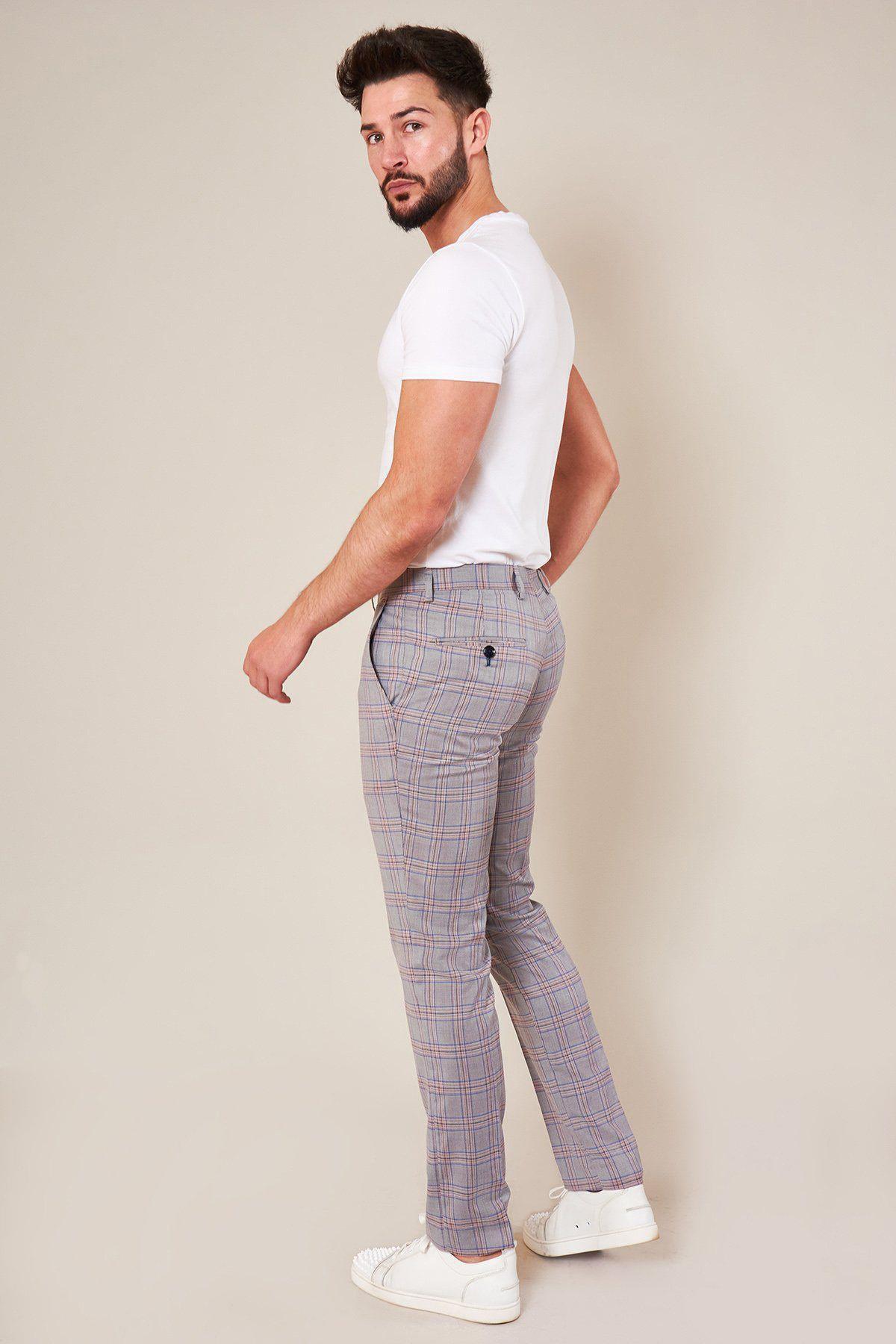 A man with a beard wears a white fitted t-shirt, Marc Darcy's ALVIN - Grey Pink Check Trousers, and white sneakers, standing and looking over his shoulder against a plain, light background.