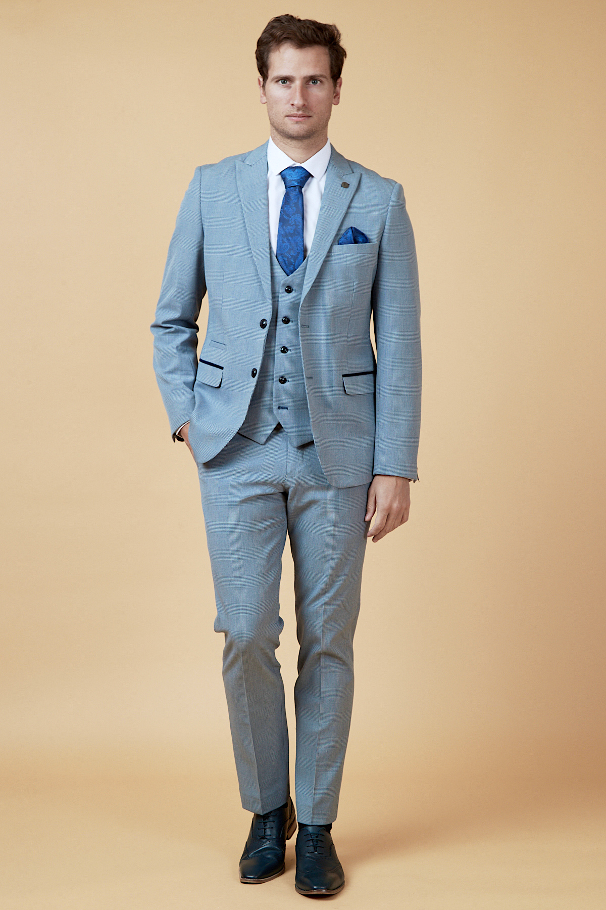 Everton midfielder James Garner wears the marcdarcy Bromley Sky Three Piece Suit with a blue tie, pocket square, white shirt, and black dress shoes against a beige background, facing forward with his left hand in his pocket.
