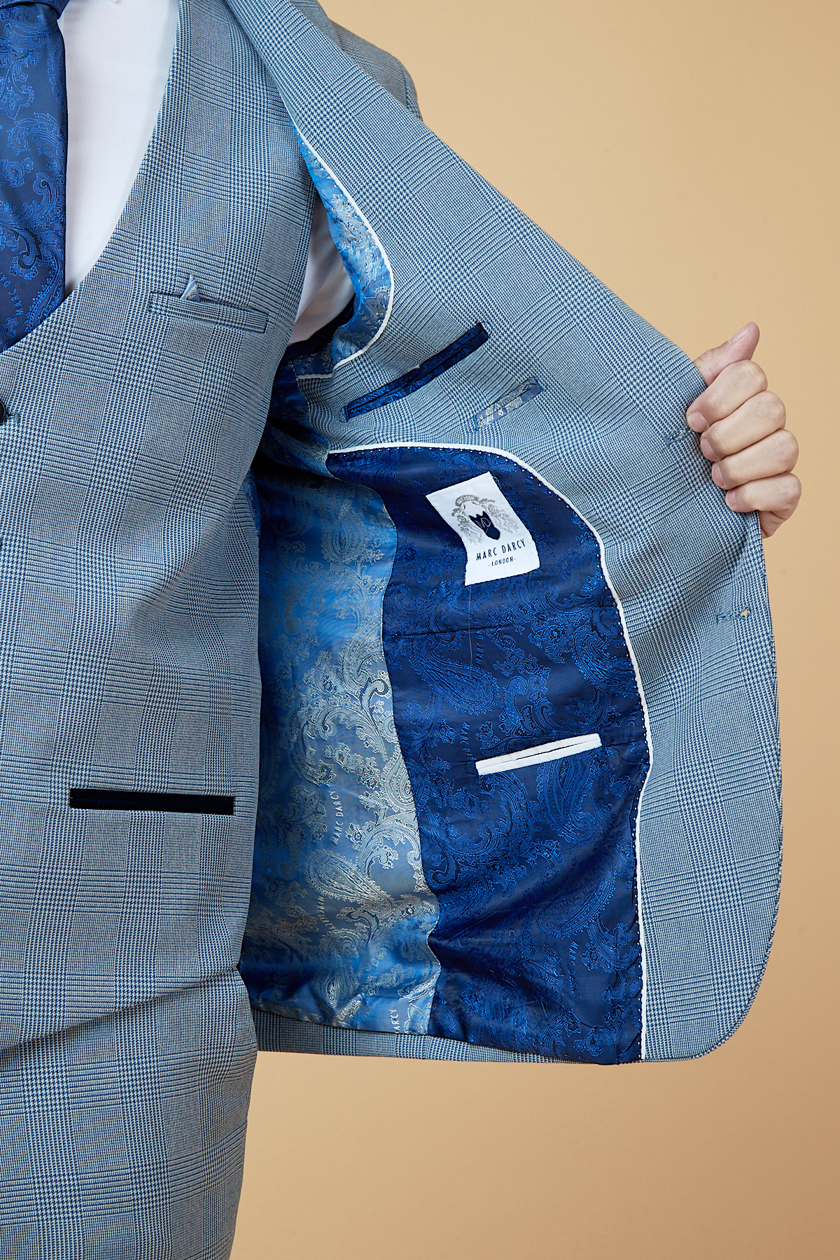 Everton midfielder James Garner wears the marcdarcy Bromley Sky Three Piece Suit, showing its blue paisley lining and white label inside. He holds open the slim fit checked jacket against a solid beige background.