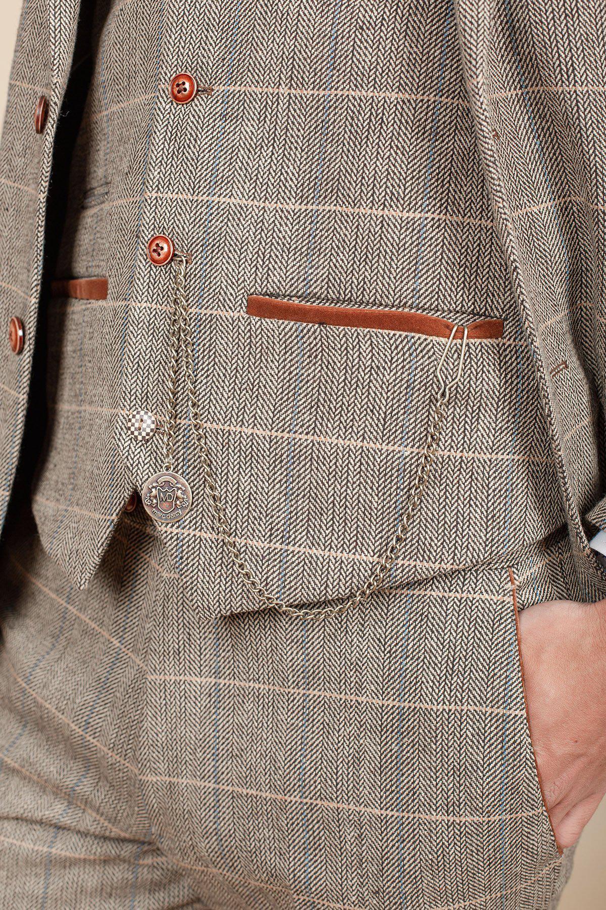 A close-up of a person wearing a Marc Darcy brown plaid suit, featuring the Antique Style Gold Plated Marc Darcy T-Bar Waistcoat Chain with an MD Velvet Keepsafe Pouch, with their hand in their pants pocket.