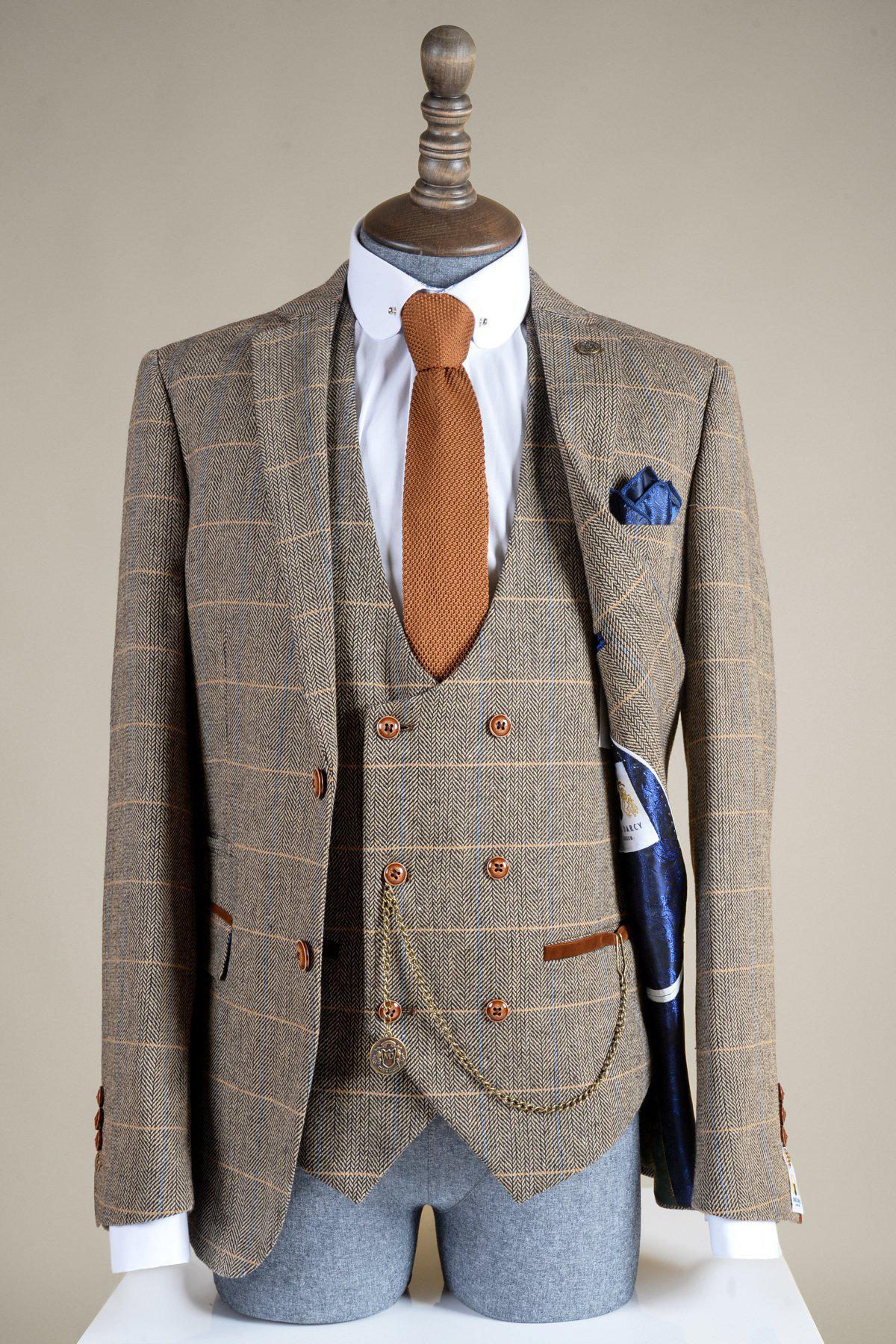 Displayed on a mannequin, the Marc Darcy antique style gold-plated T-bar waistcoat chain with MD velvet keepsafe pouch complements a brown plaid three-piece suit paired with a white shirt, brown textured tie, blue pocket square, and brown buttons.
