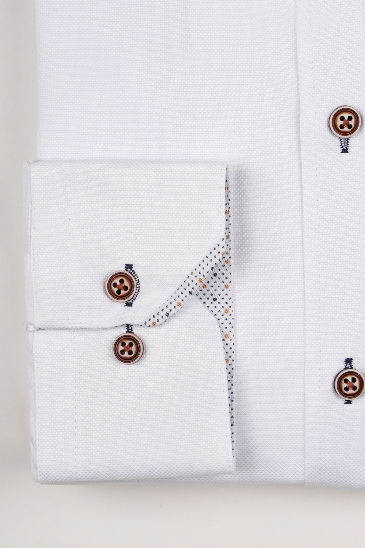 A close-up of the Marc Darcy ARCHIE White Grandad Collar Shirt shows tan buttons, blue stitching, and a dotted inner cuff. Neatly folded against a light backdrop, it offers a modern, casual vibe.