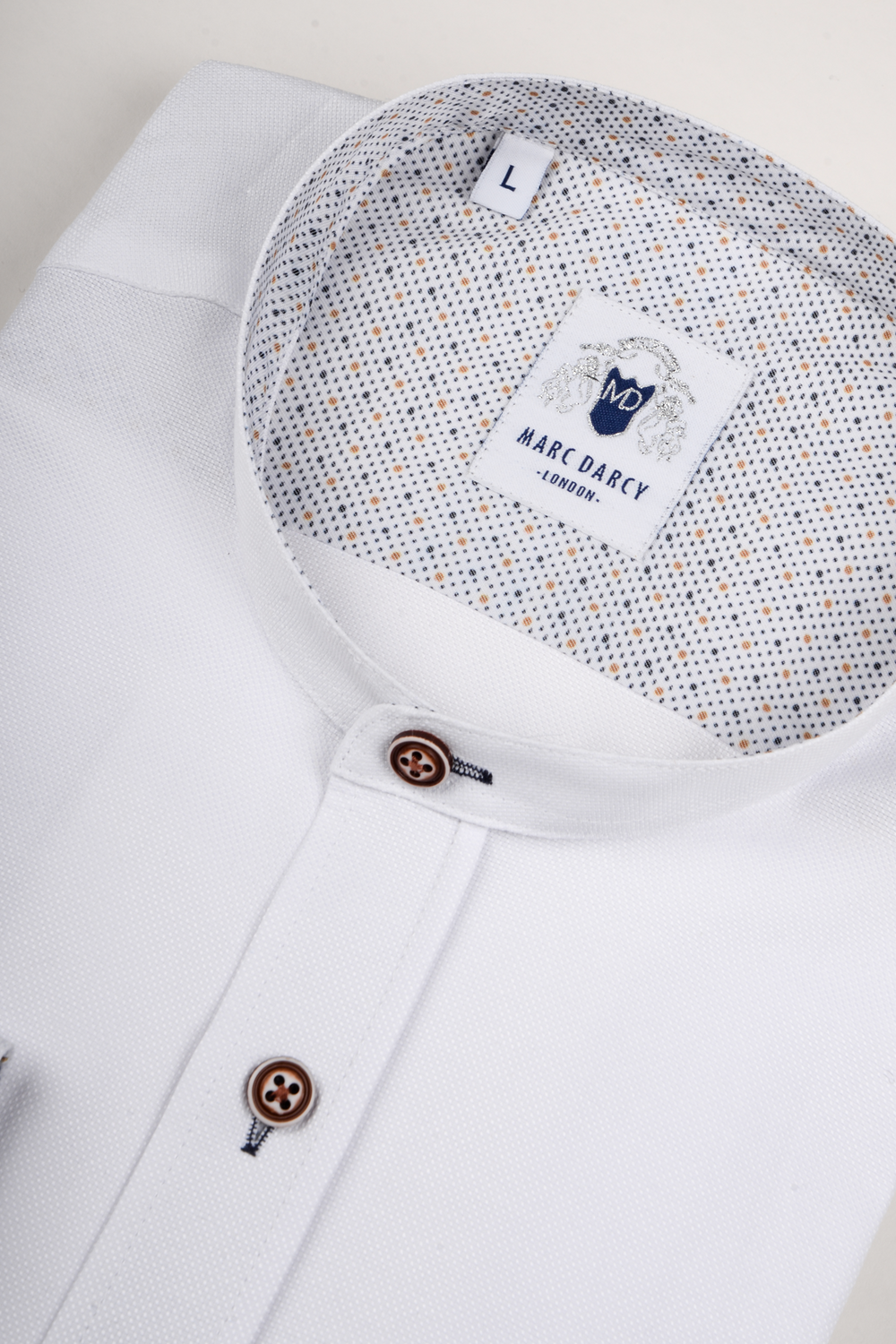 A neatly folded Marc Darcy ARCHIE white grandad collar shirt with tan buttons and a patterned inner collar, size L. The label shows the Marc Darcy logo and “London,” creating a relaxed, casual vibe.